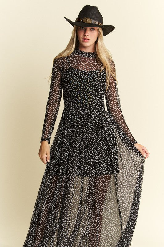 Woman wearing black Hendrix long sleeve animal print mesh maxi dress with sheer skirt and black wide-brimmed hat against beige background