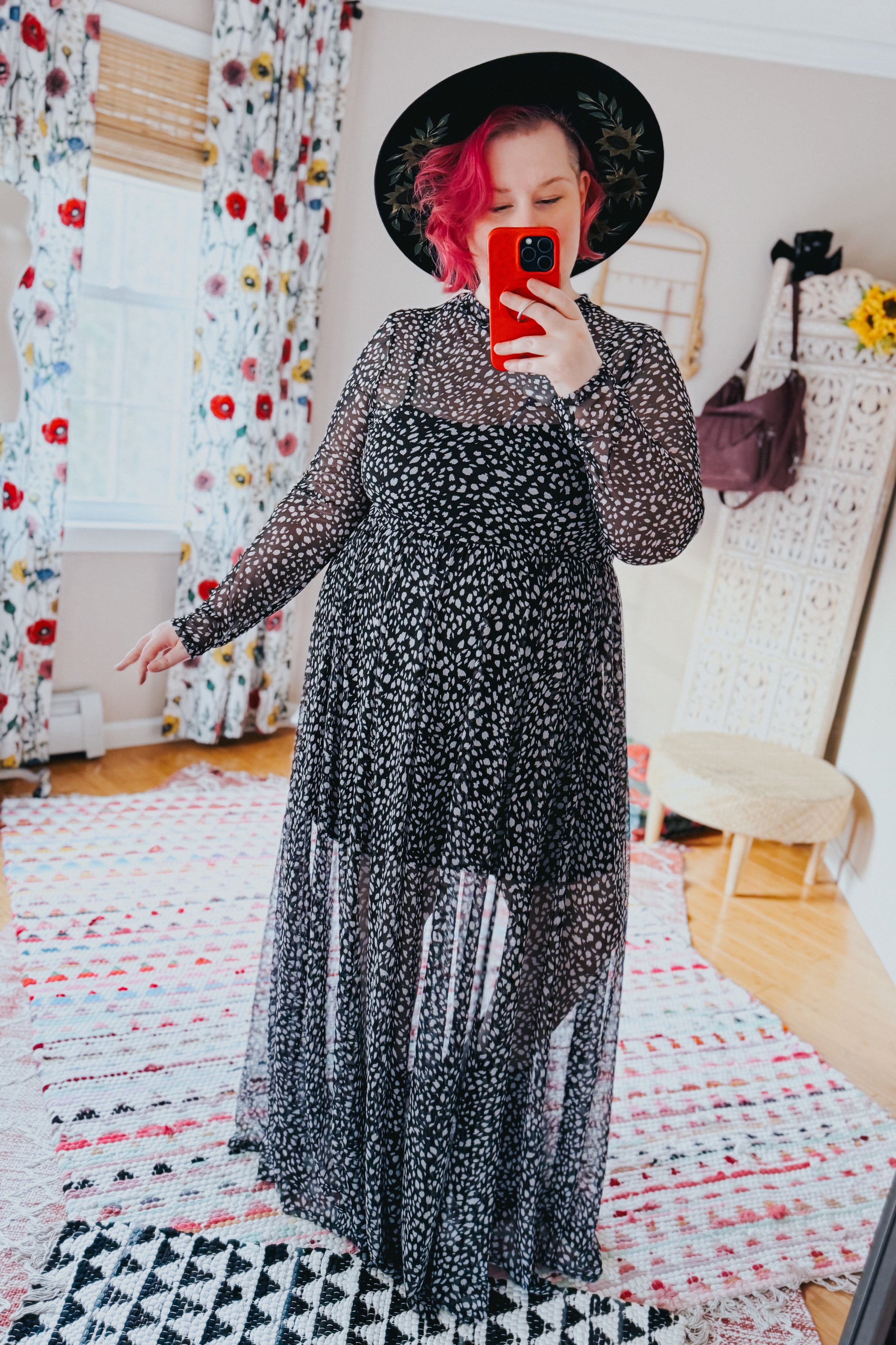 Woman taking selfie indoors wearing black Hendrix long sleeve animal print mesh maxi dress and black wide-brim hat