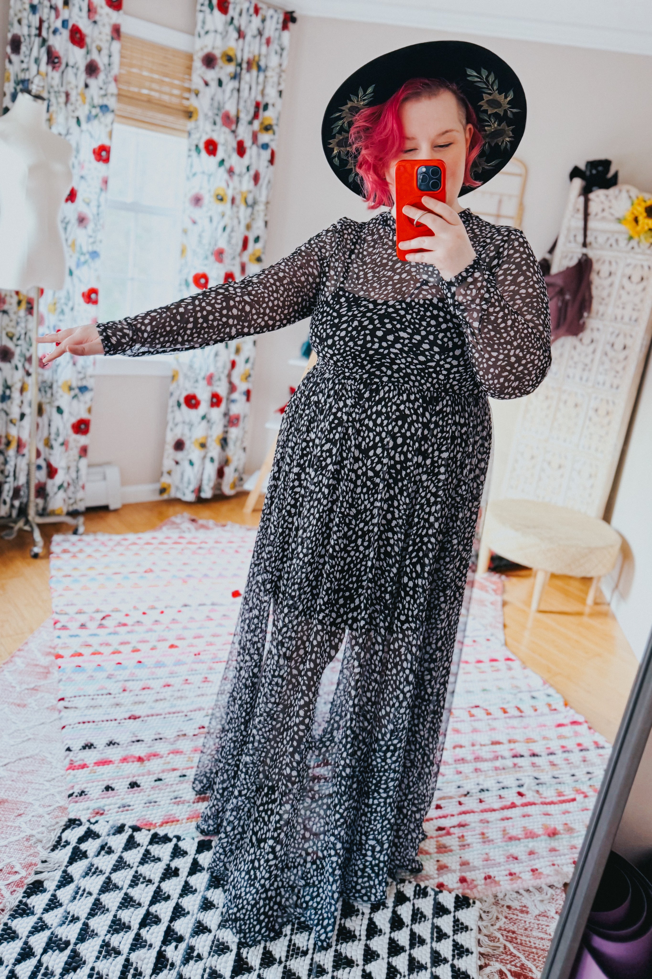Woman taking mirror selfie indoors wearing black Hendrix long sleeve animal print mesh maxi dress and black floral hat