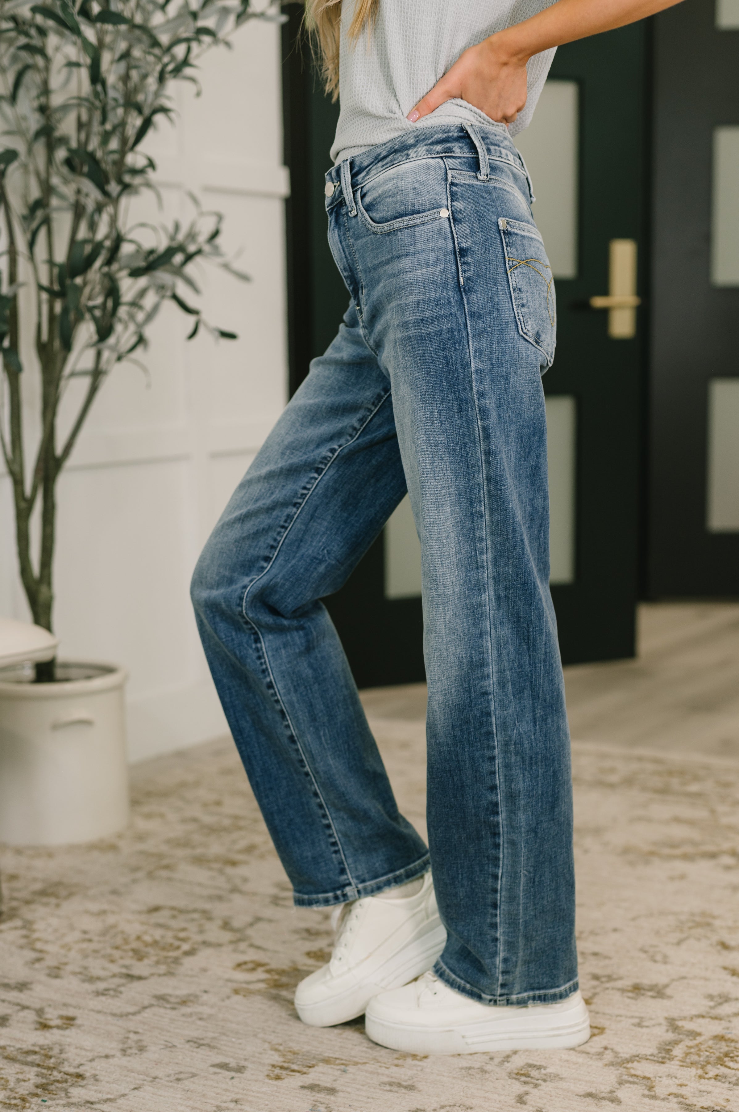 Side view of woman wearing mid rise blue straight jeans with white sneakers in cozy indoor setting