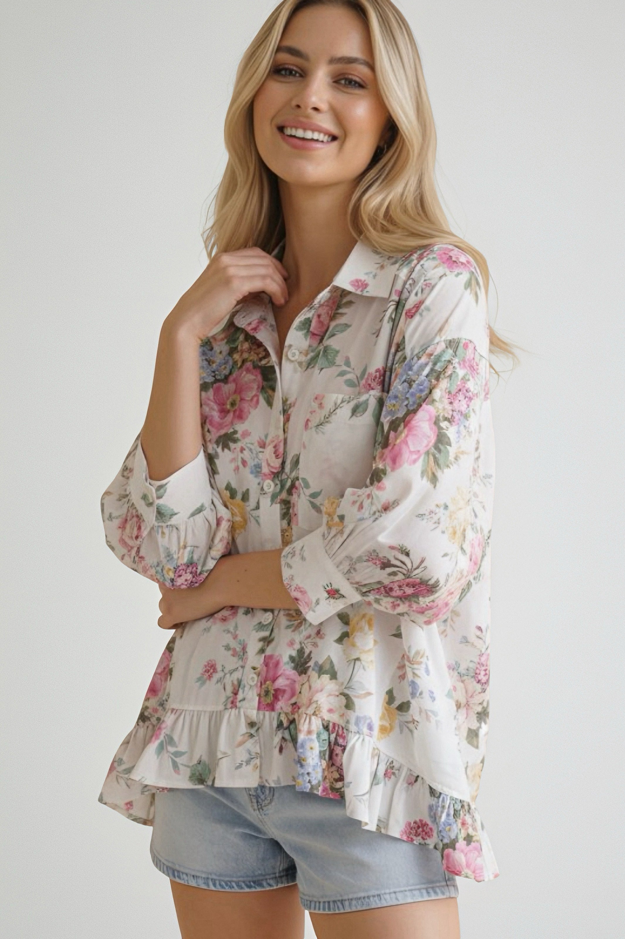 Woman wearing an ivory floral blouse with puffed three-quarter sleeves and ruffled hem paired with light denim shorts
