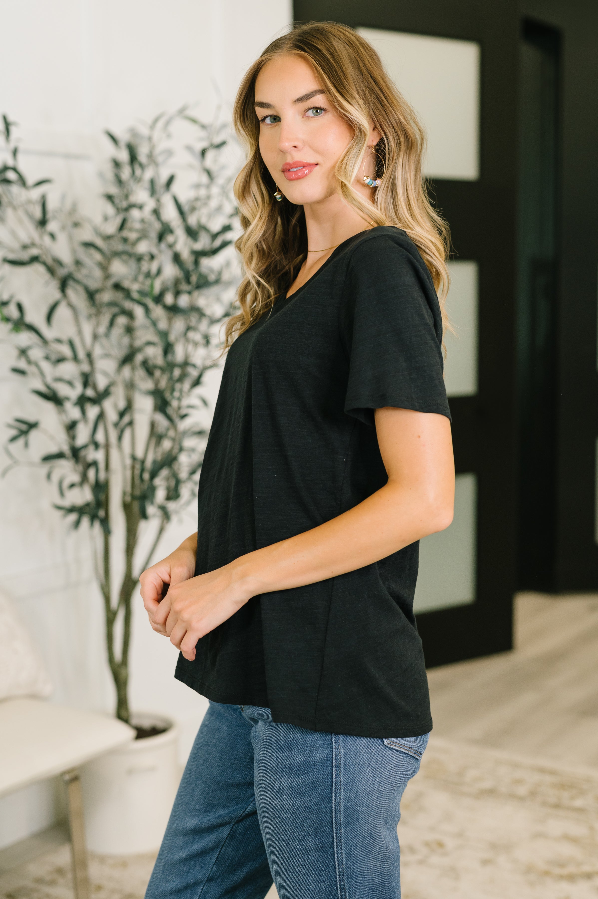 Woman wearing relaxed fit black V-neck tee with short sleeves and blue jeans standing indoors