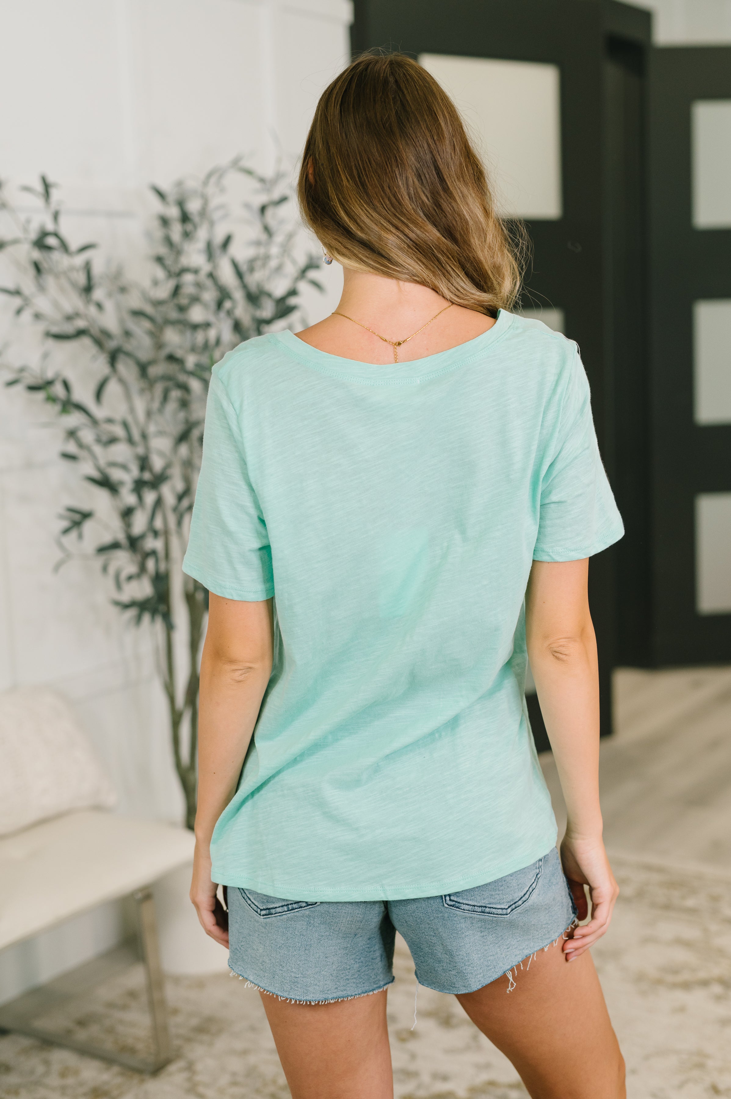 Woman wearing relaxed fit mint heathered V-neck tee paired with frayed denim shorts indoors