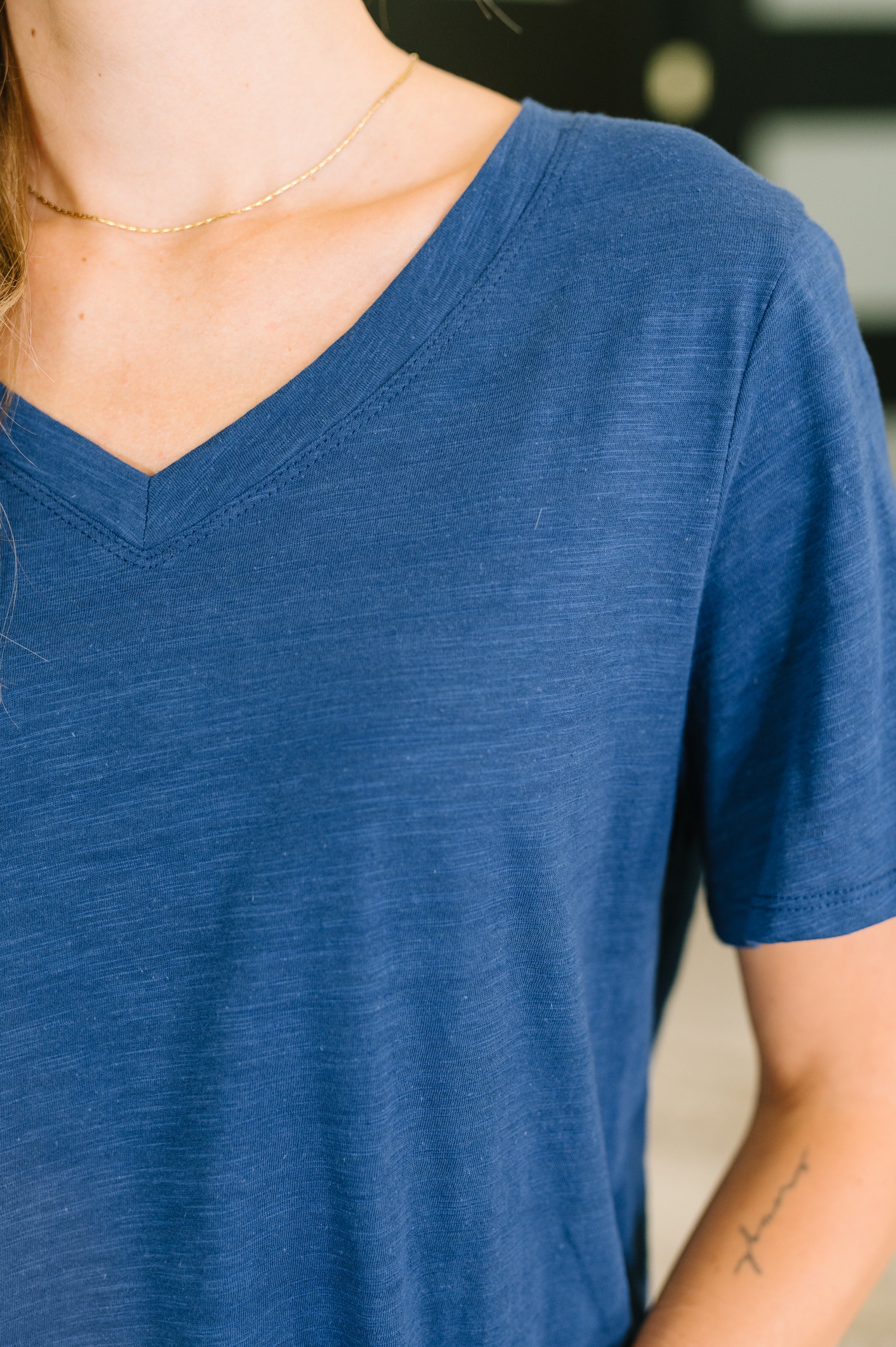 Close-up of soft navy v-neck tee with short sleeves worn with delicate gold chain necklace on woman indoors