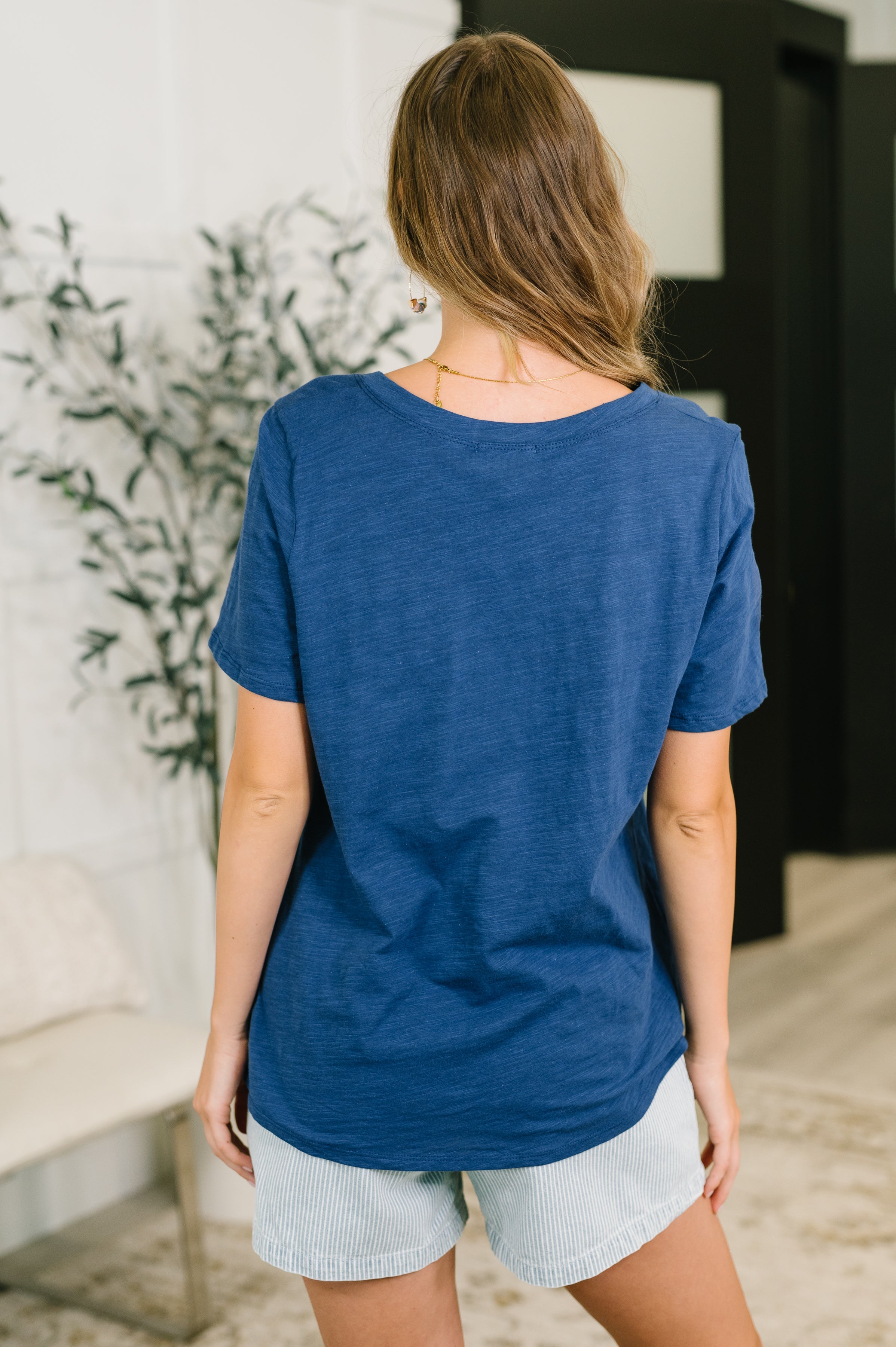 Rear view of woman wearing relaxed navy short sleeve tee paired with light striped shorts indoors