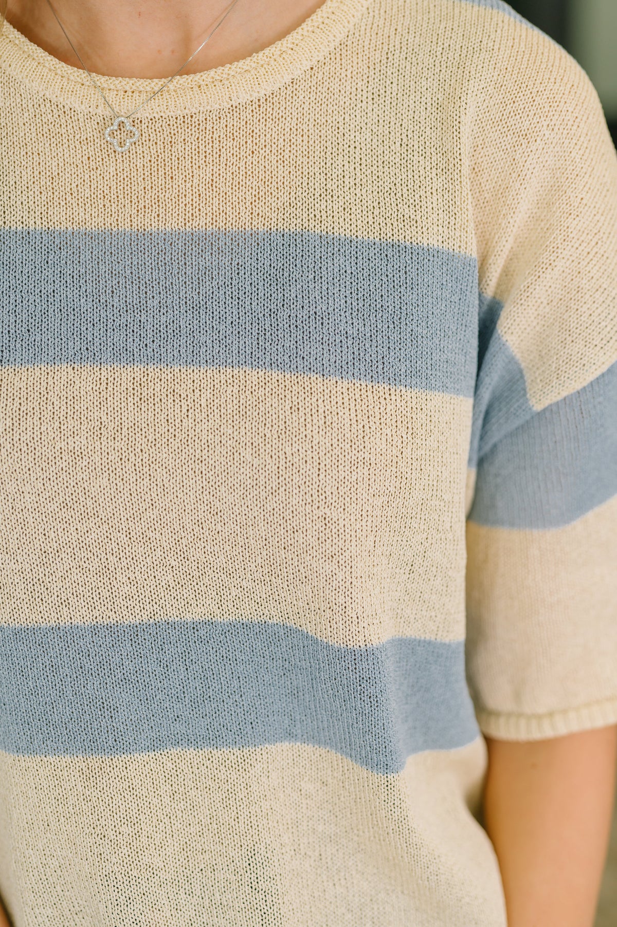 Woman wearing a beige lightweight knit top with blue horizontal stripes short sleeves and a round neckline close up