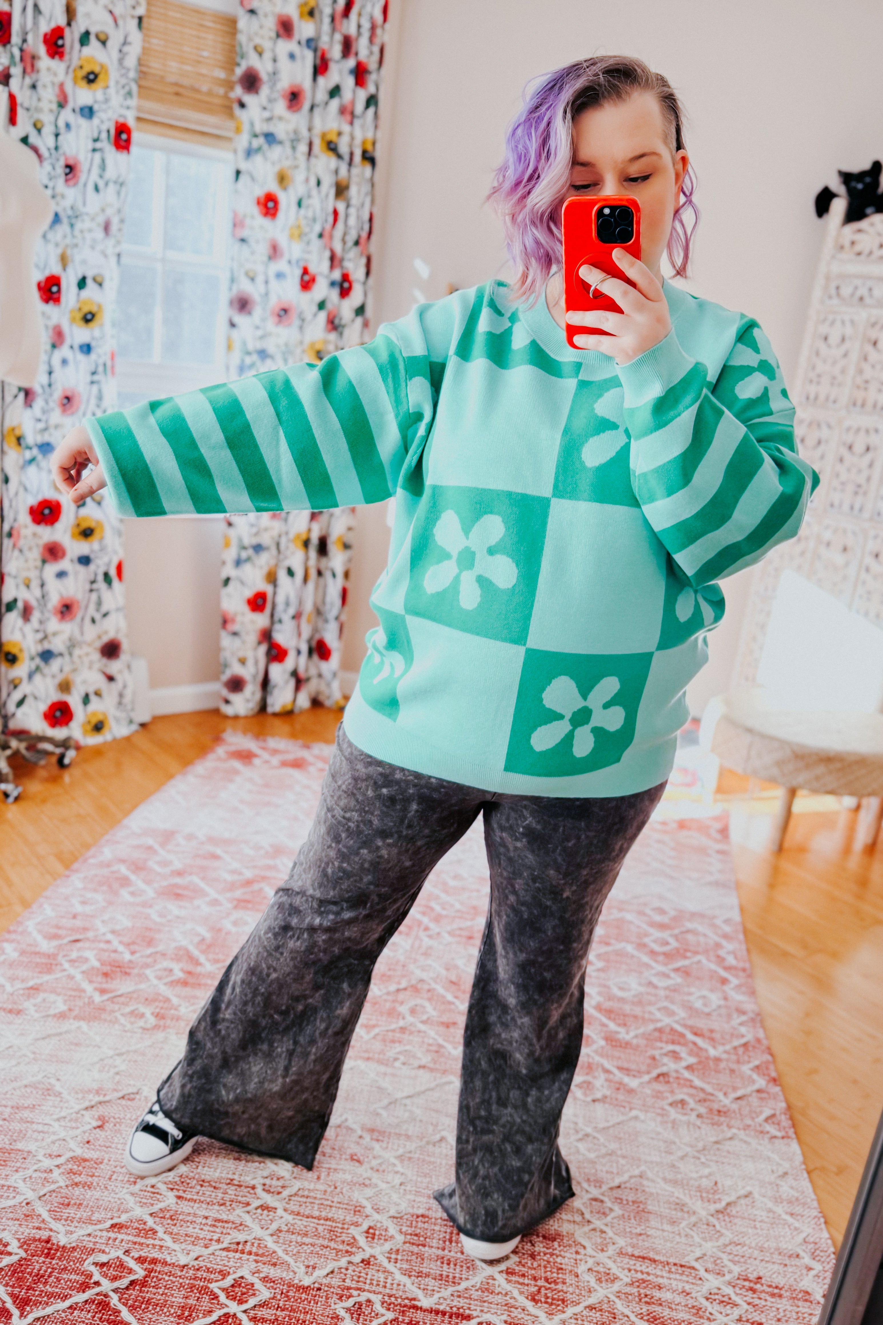 Woman wearing a checkered floral print mint sweater over acid wash flared pants in an indoor setting.