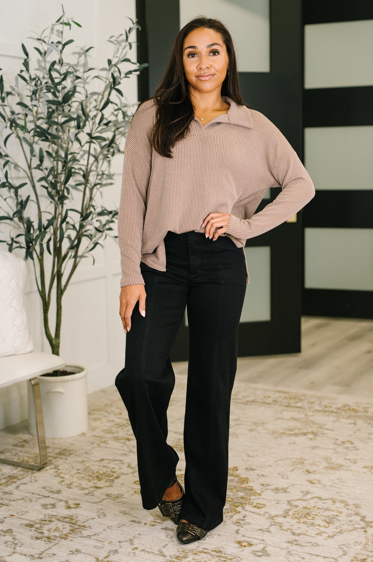 Woman modeling a mocha textured collared pullover with relaxed sleeves and black wide leg pants in a modern home interior