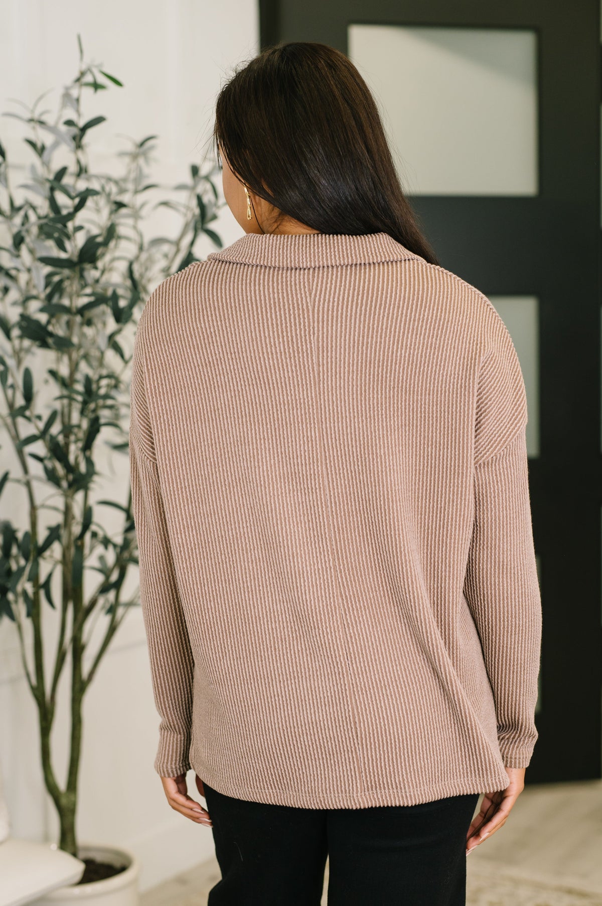 Back view of a woman wearing a mocha textured ribbed collared pullover with relaxed sleeves and black pants indoors