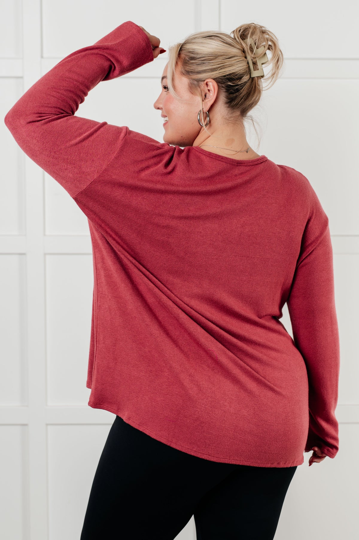 Woman viewed from behind wearing a cranberry brushed Hacci long sleeve top with a relaxed fit and black leggings against a paneled wall