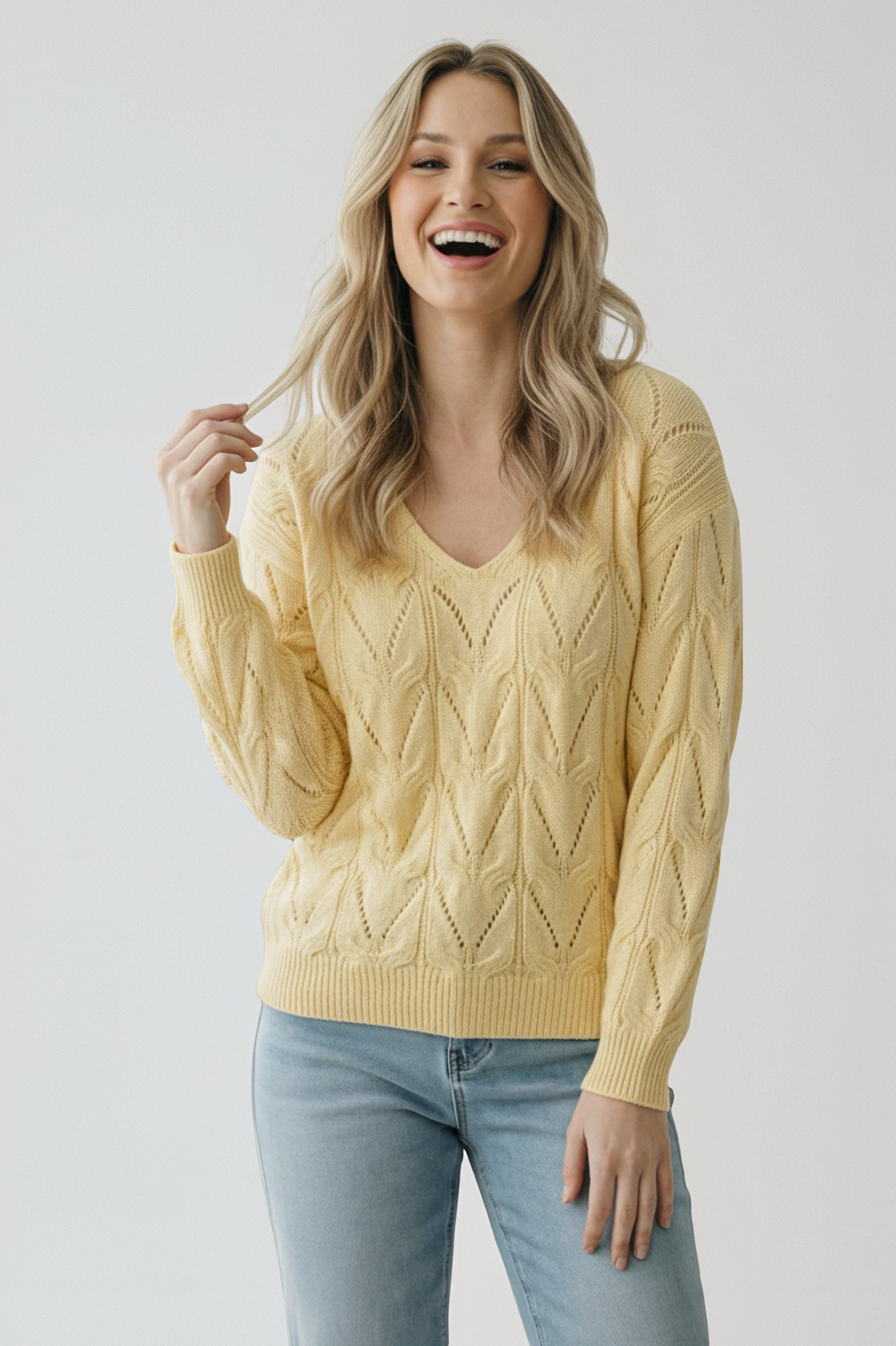 Smiling woman wearing a yellow knit v-neck sweater with a textured pattern paired with light blue jeans