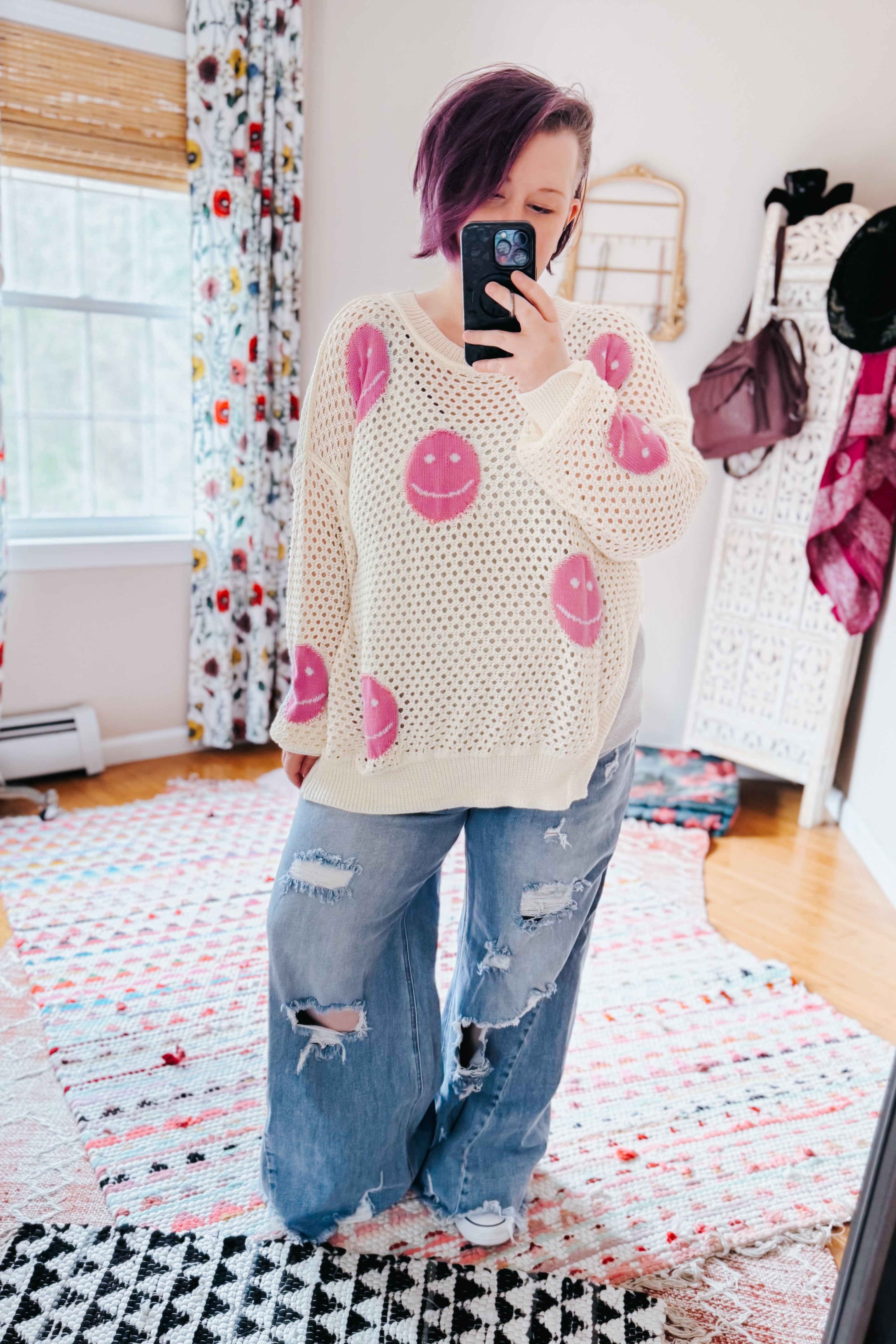 Woman taking mirror selfie wearing beige and pink In My Feelings Smiley Open Knit Top with ripped wide-leg jeans in bright cozy room