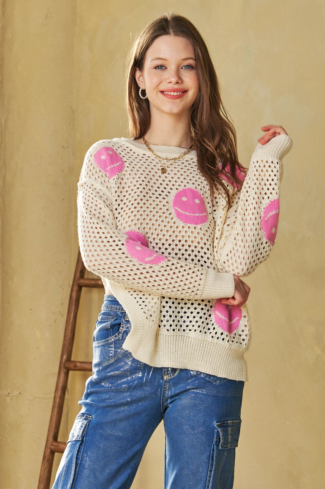 Young woman wearing beige and pink In My Feelings Smiley Open Knit Top with relaxed fit blue cargo jeans indoors