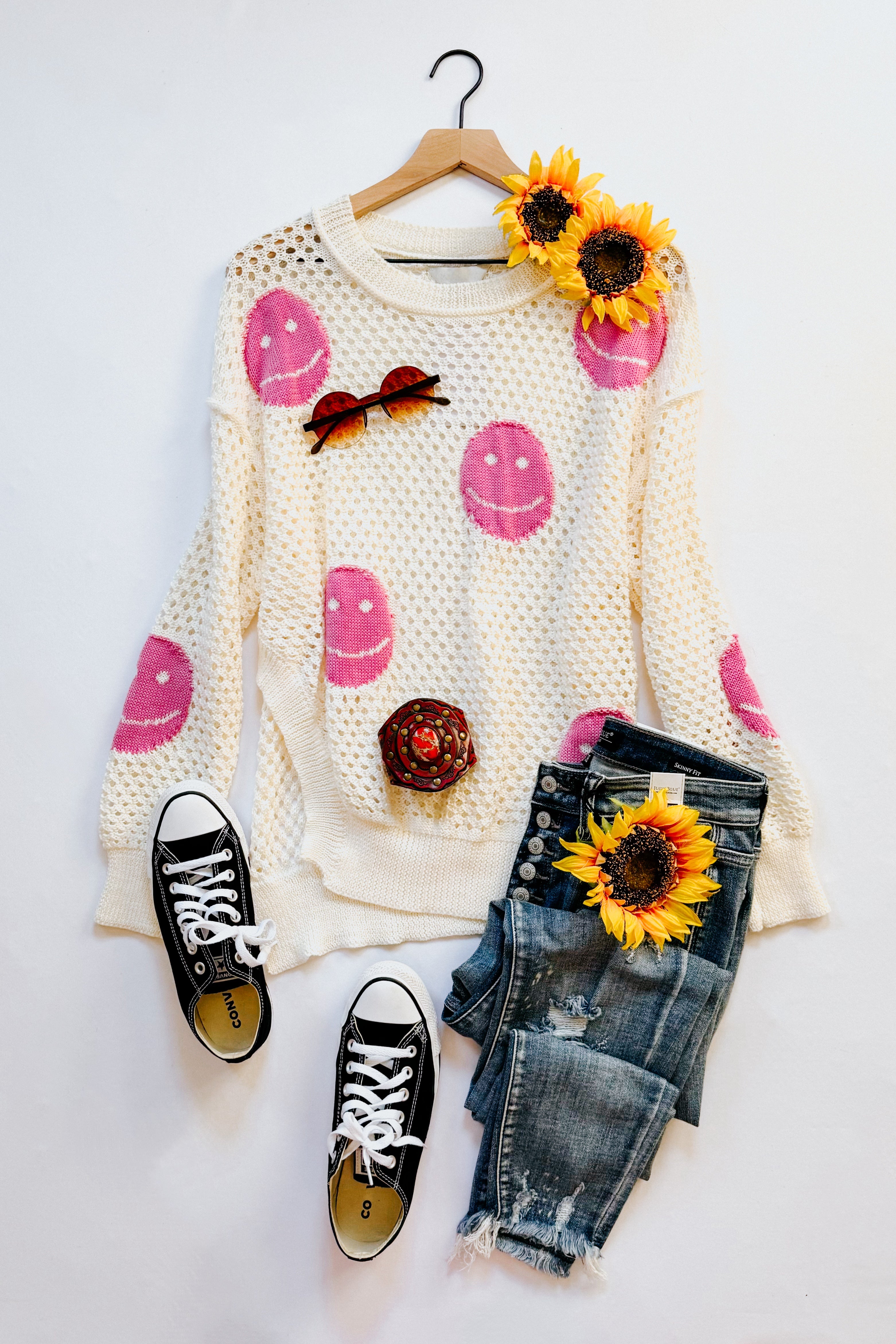 Beige and pink In My Feelings Smiley Open Knit Top with distressed jeans and black sneakers styled with sunflowers and sunglasses