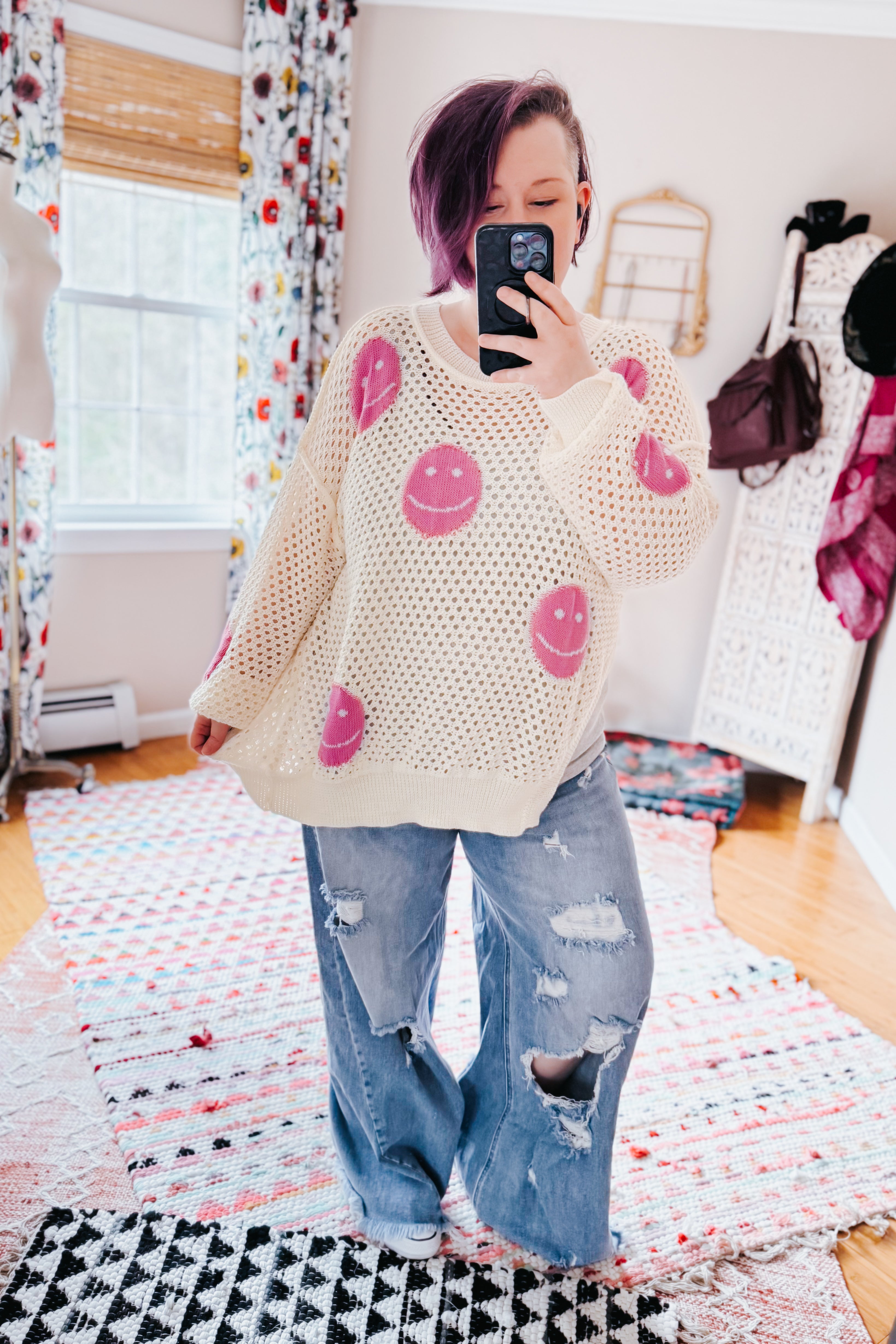 Women wearing beige and pink In My Feelings Smiley Open Knit Top with distressed wide-leg jeans in bright room mirror selfie