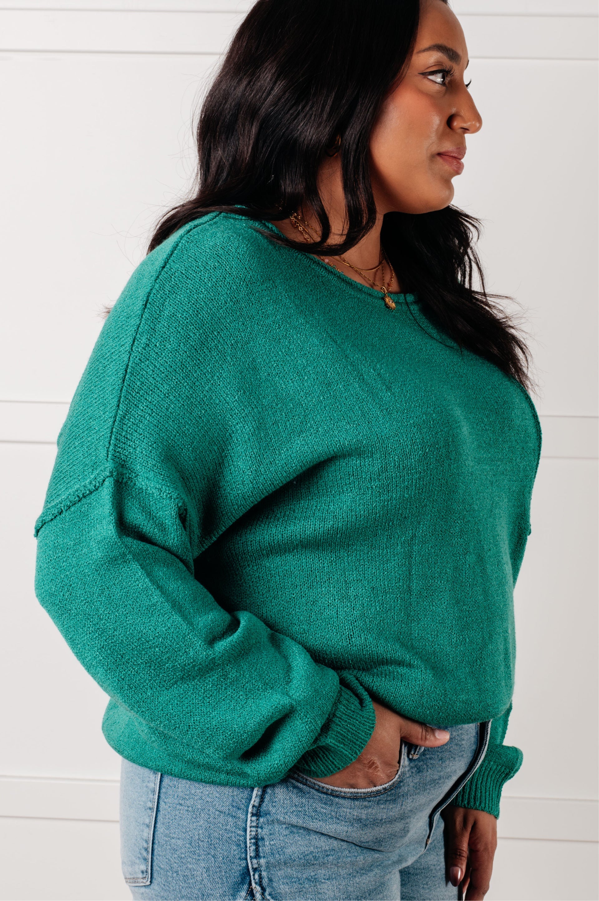 Side profile of woman wearing green In Stitches Drop Shoulder Sweater with light blue jeans against white background