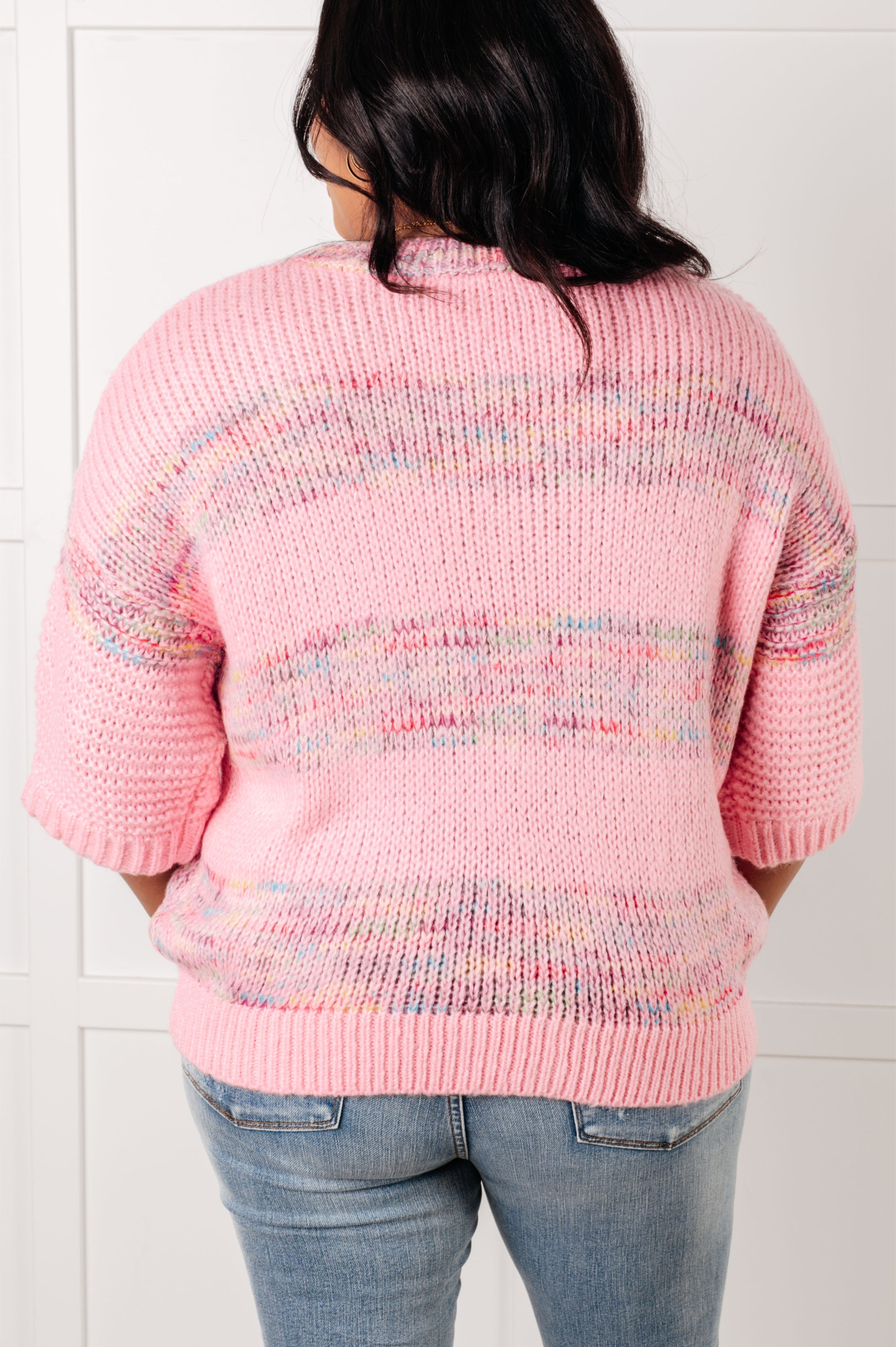 Woman seen from behind wearing pink In the Cards Striped Sweater with short sleeves and light wash jeans against a white background