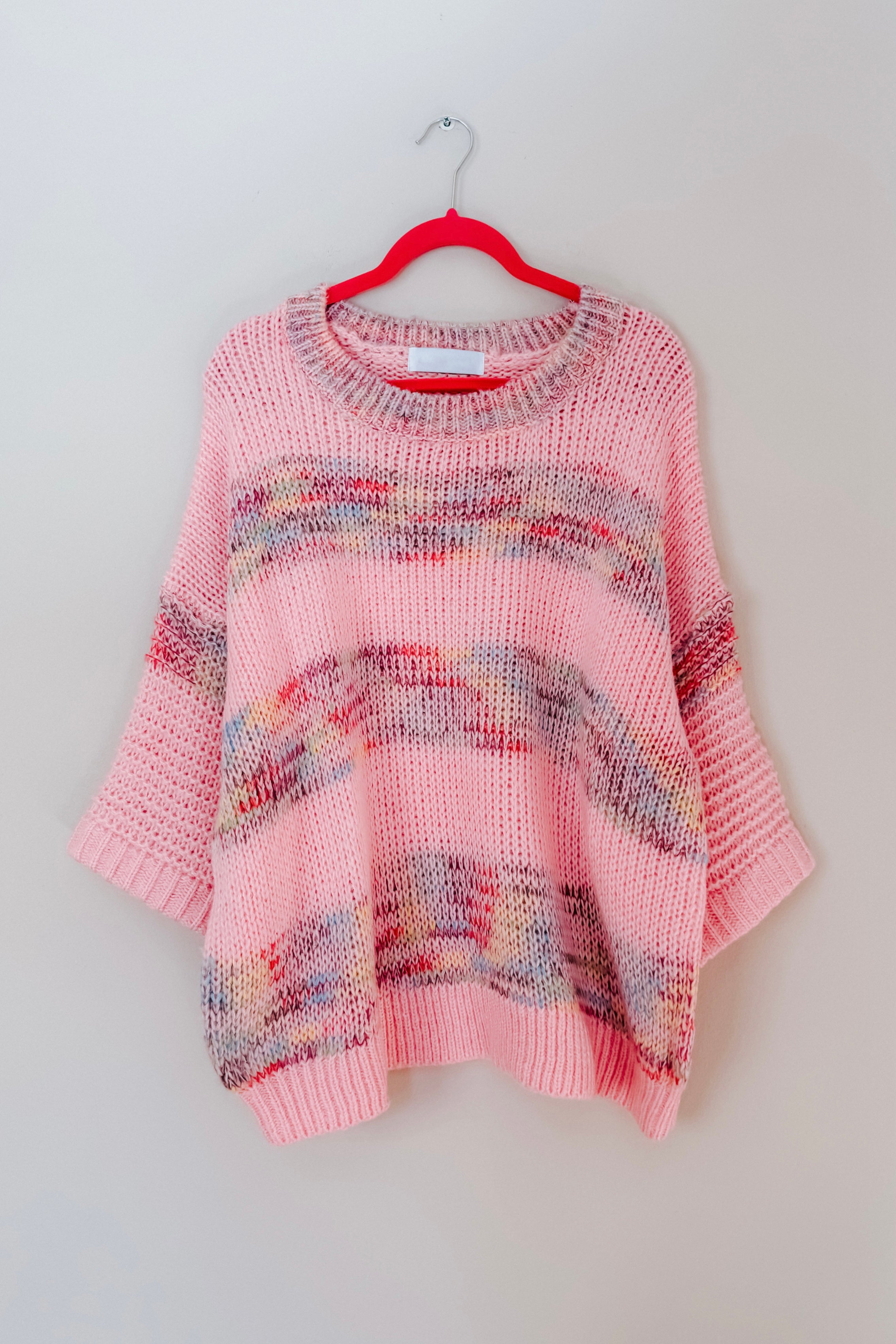 Pink In the Cards Striped Sweater with wide knit and blended multicolor stripes hanging on red hanger against neutral background