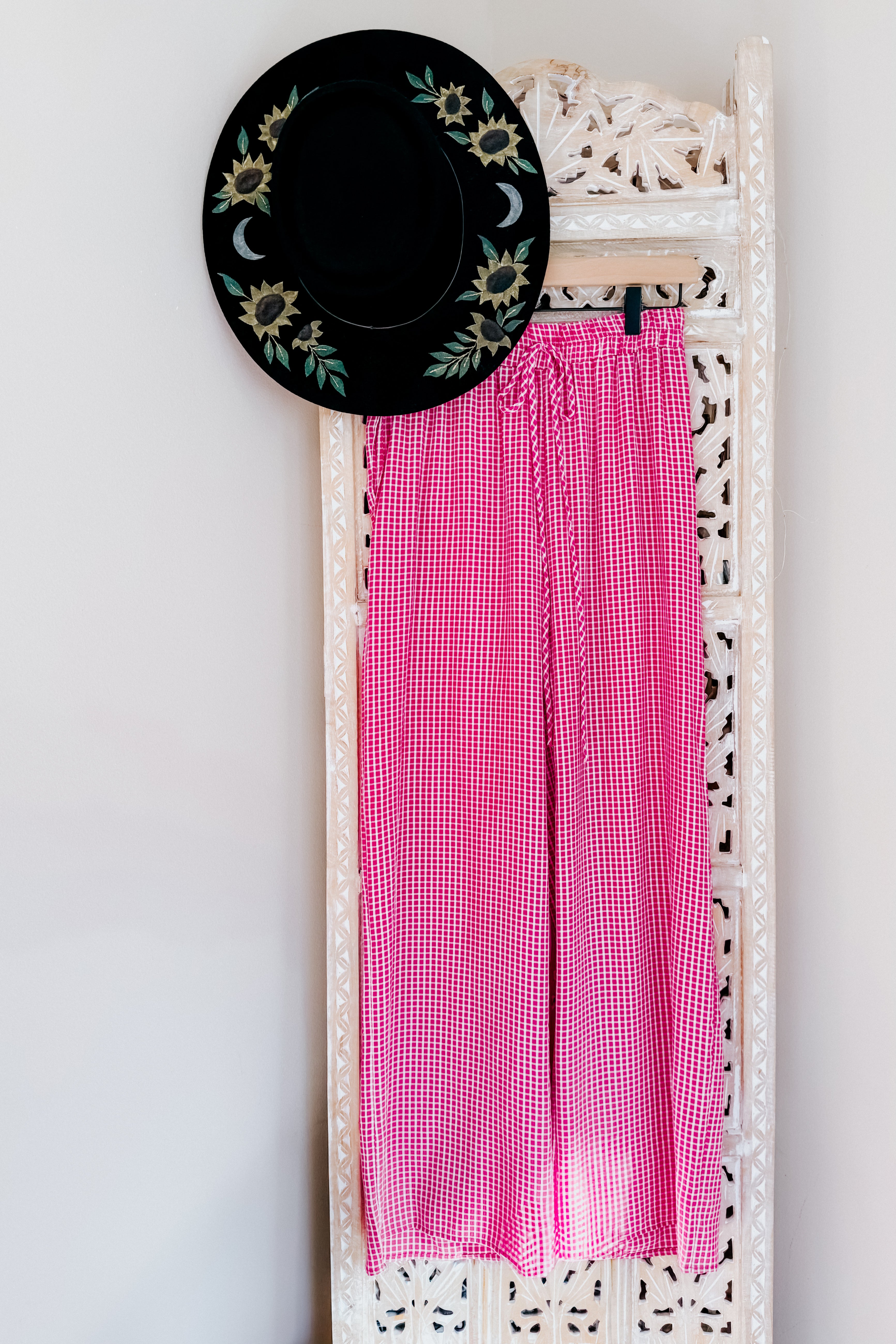 Pink In The Groove Checkered Print Pants with relaxed fit and drawstring waist hanging on ornate carved screen with black embroidered hat