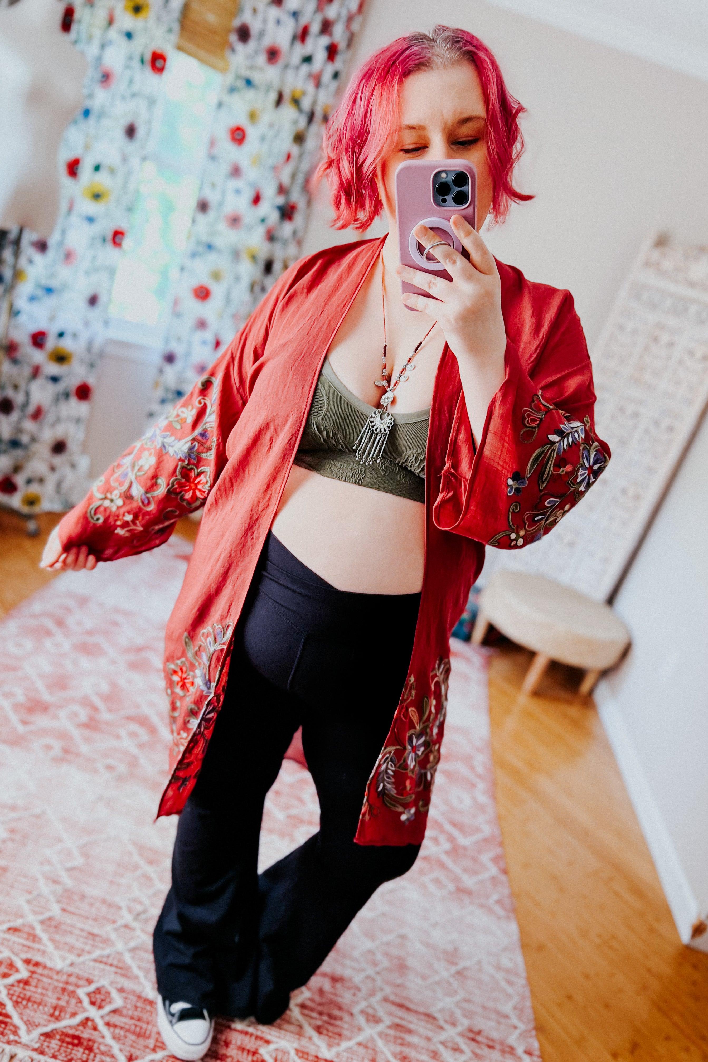 Woman taking selfie wearing crimson In The Meadow embroidered duster over olive bralette and black pants indoors