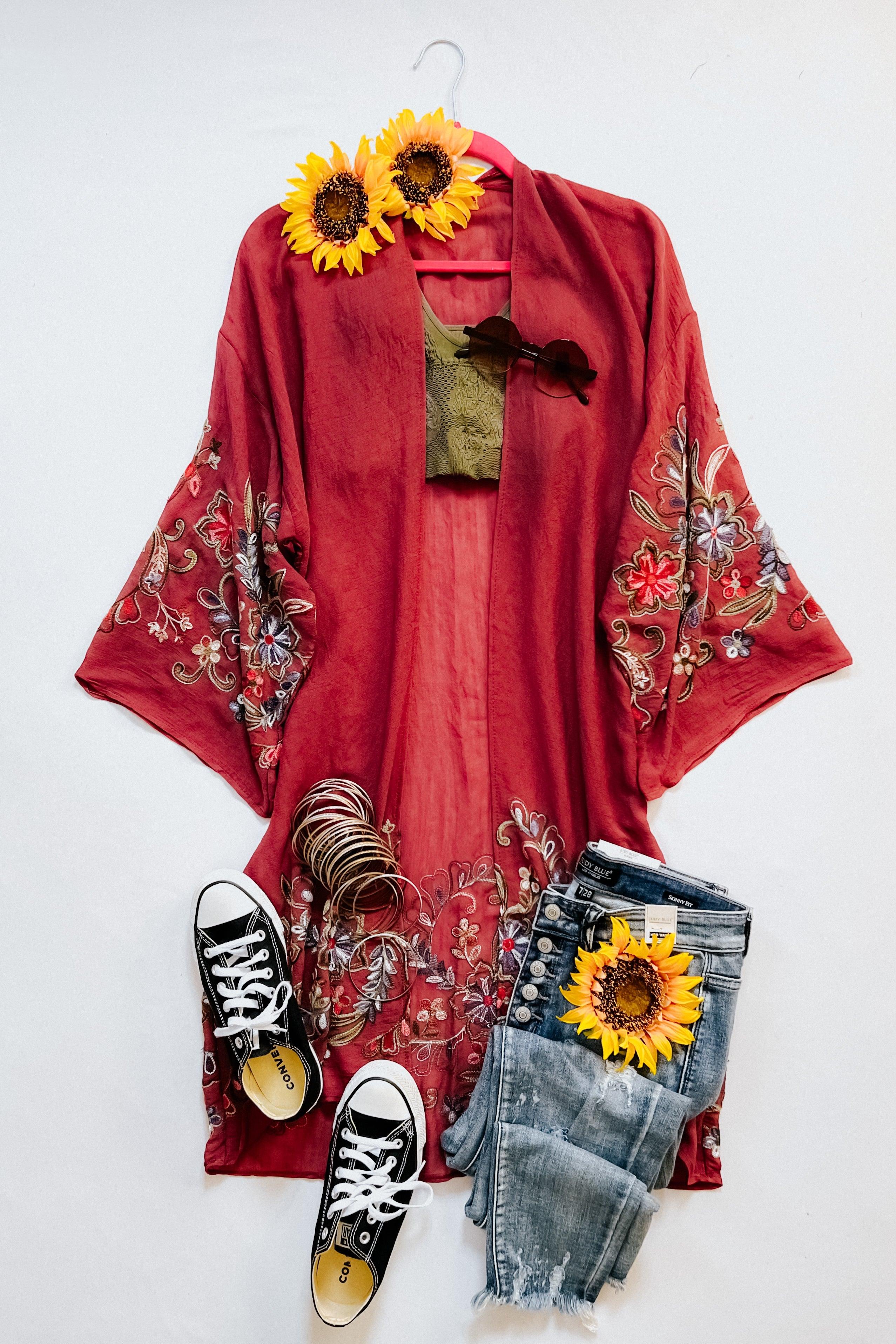 Crimson In The Meadow embroidered duster with floral designs paired with distressed blue jeans, black sneakers, and sunflower accessories