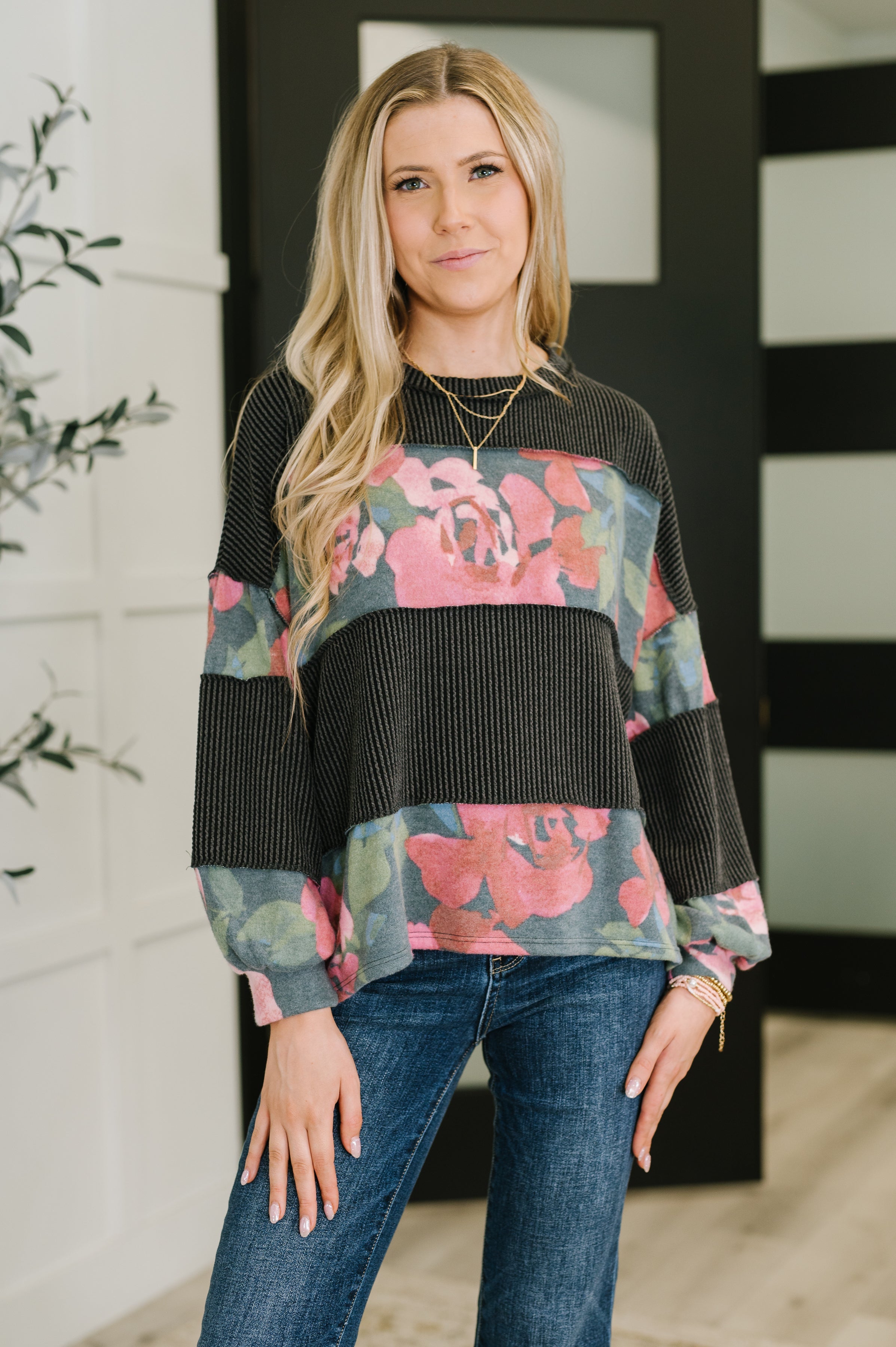 Woman wearing black pullover with wide pink floral contrast stripes paired with blue jeans indoors