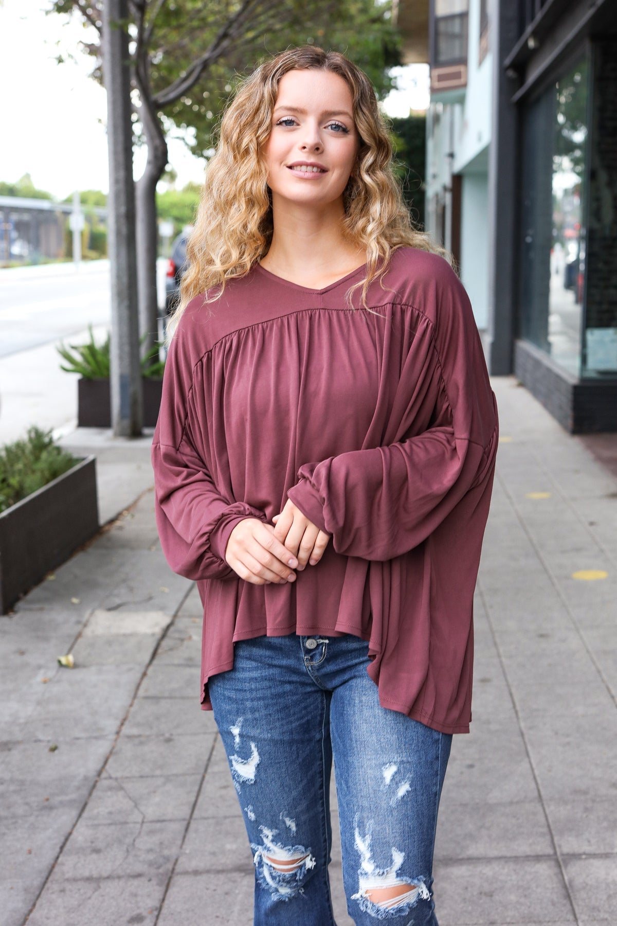 Woman wearing wine In This Groove modal knit top with relaxed fit and gathered yoke paired with distressed blue jeans outdoors
