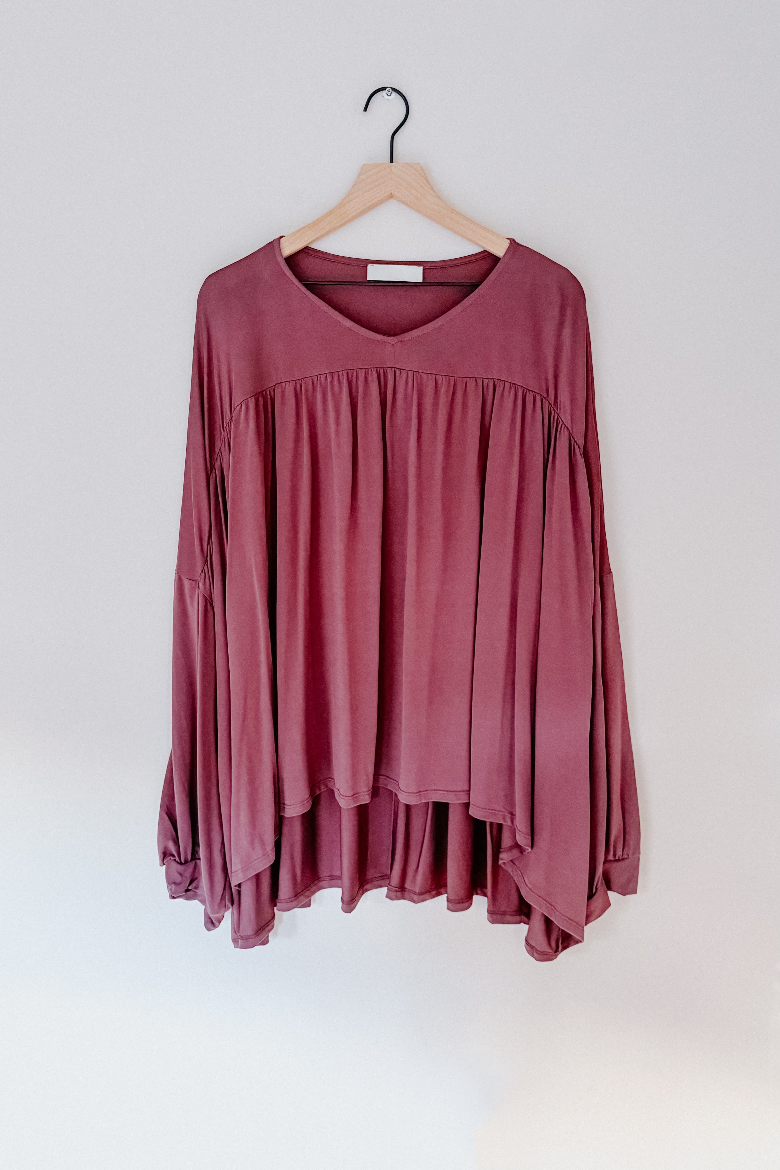 Wine-colored In This Groove modal knit top with gathered fabric detail and long sleeves hanging on wooden hanger against white wall