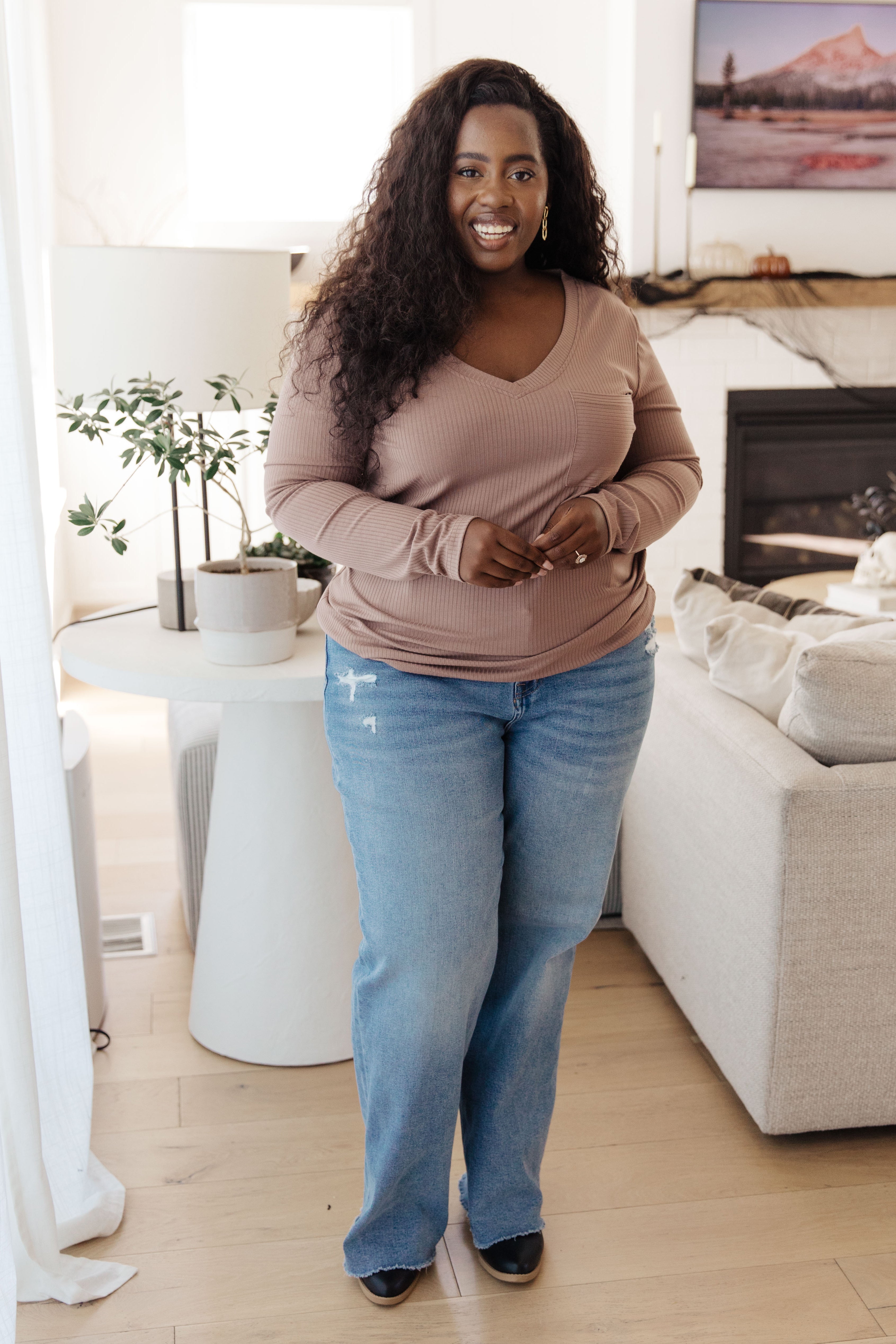 Smiling woman wearing taupe Indeed You Do long sleeve V-neck top with ribbed texture and light blue jeans indoors