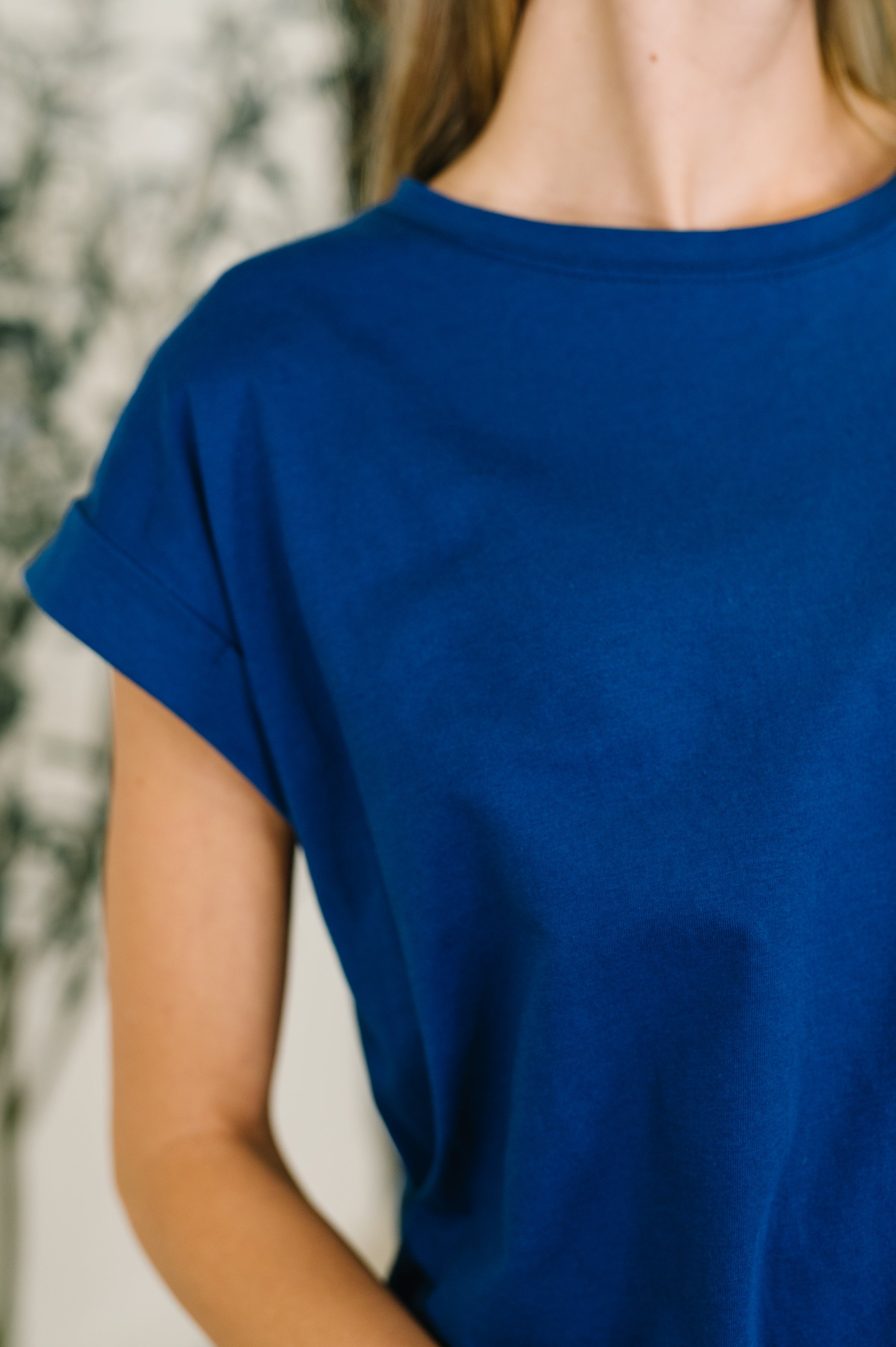 Close-up of woman wearing a blue basic rolled sleeve tee with a round neckline indoors