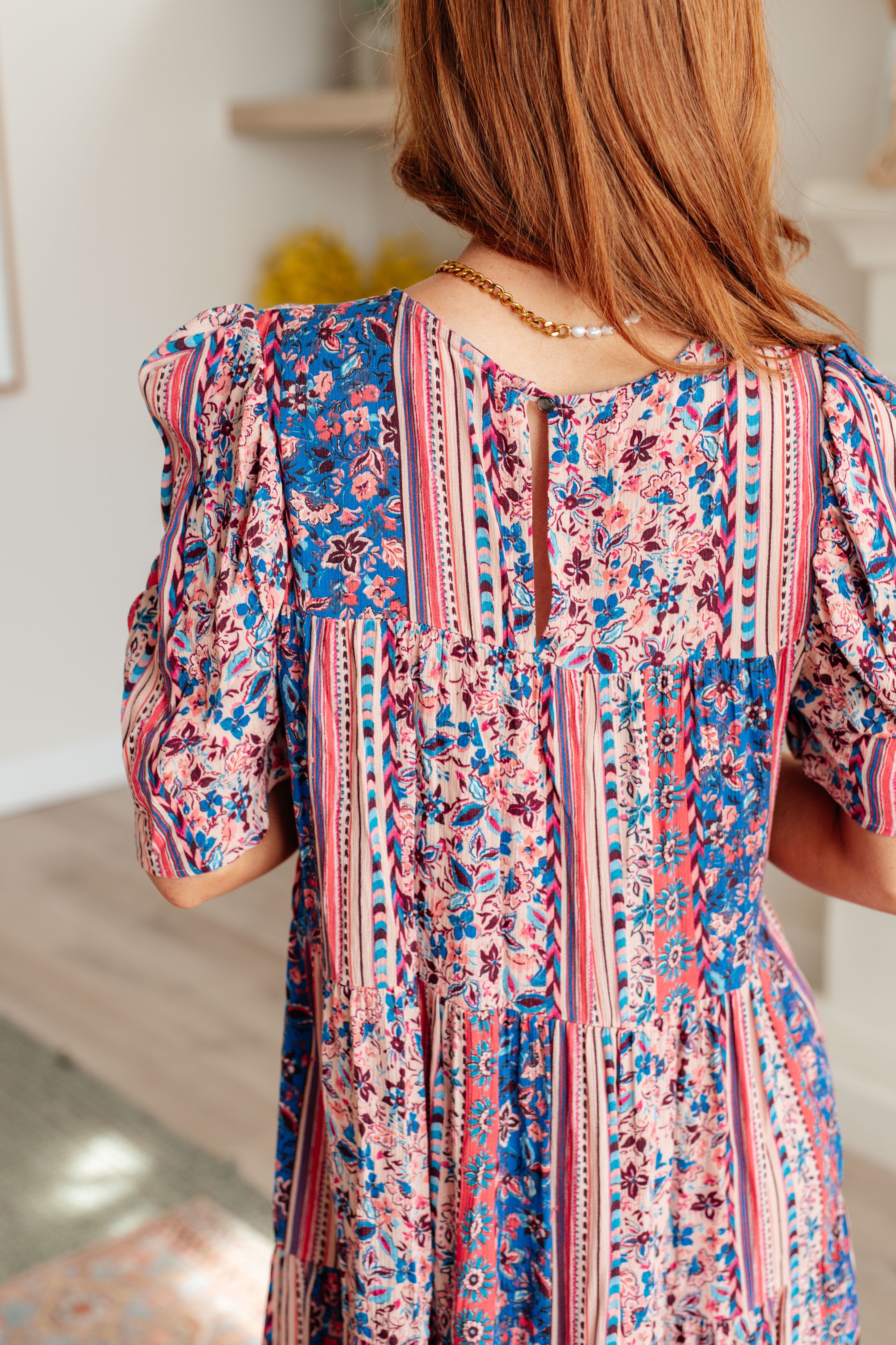 Back view of woman wearing a pink and blue patterned dress with puffed sleeves and a keyhole neckline detail