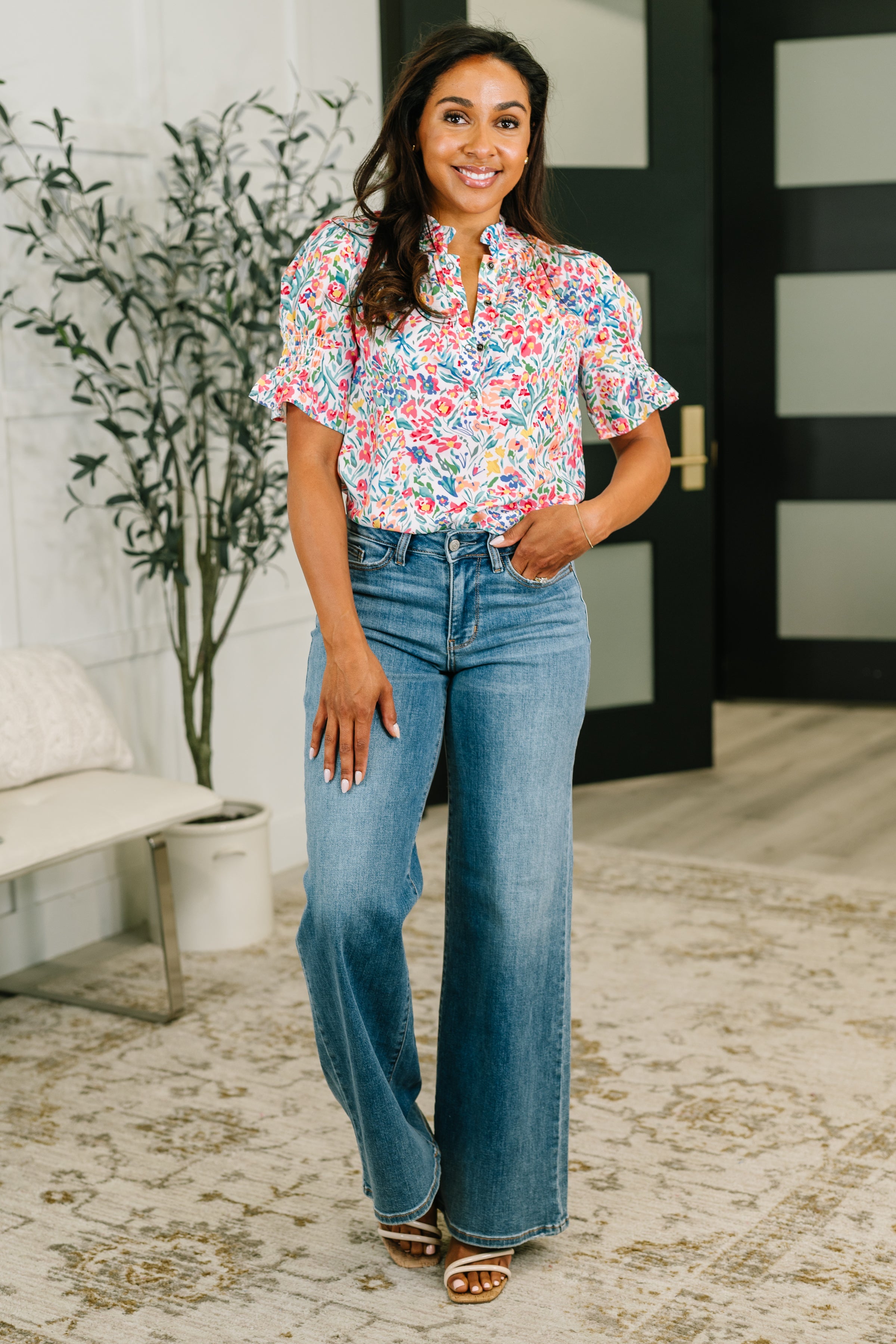 Woman wearing a floral split neck blouse with puffed sleeves paired with high-waisted wide-leg jeans in eclectic space