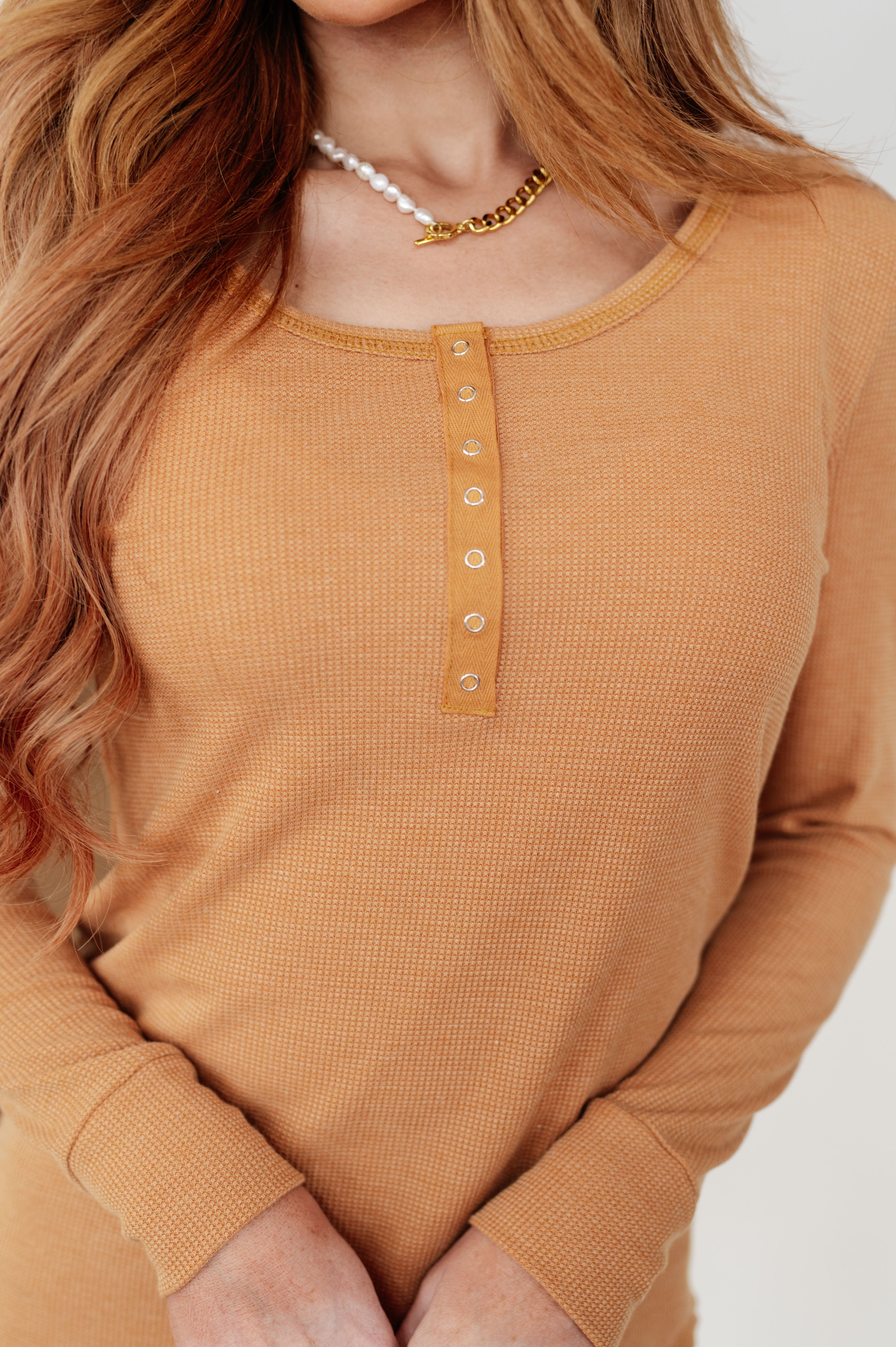 Close-up of golden sand baby waffle knit long sleeve top with snap button placket and scoop neckline on model indoors
