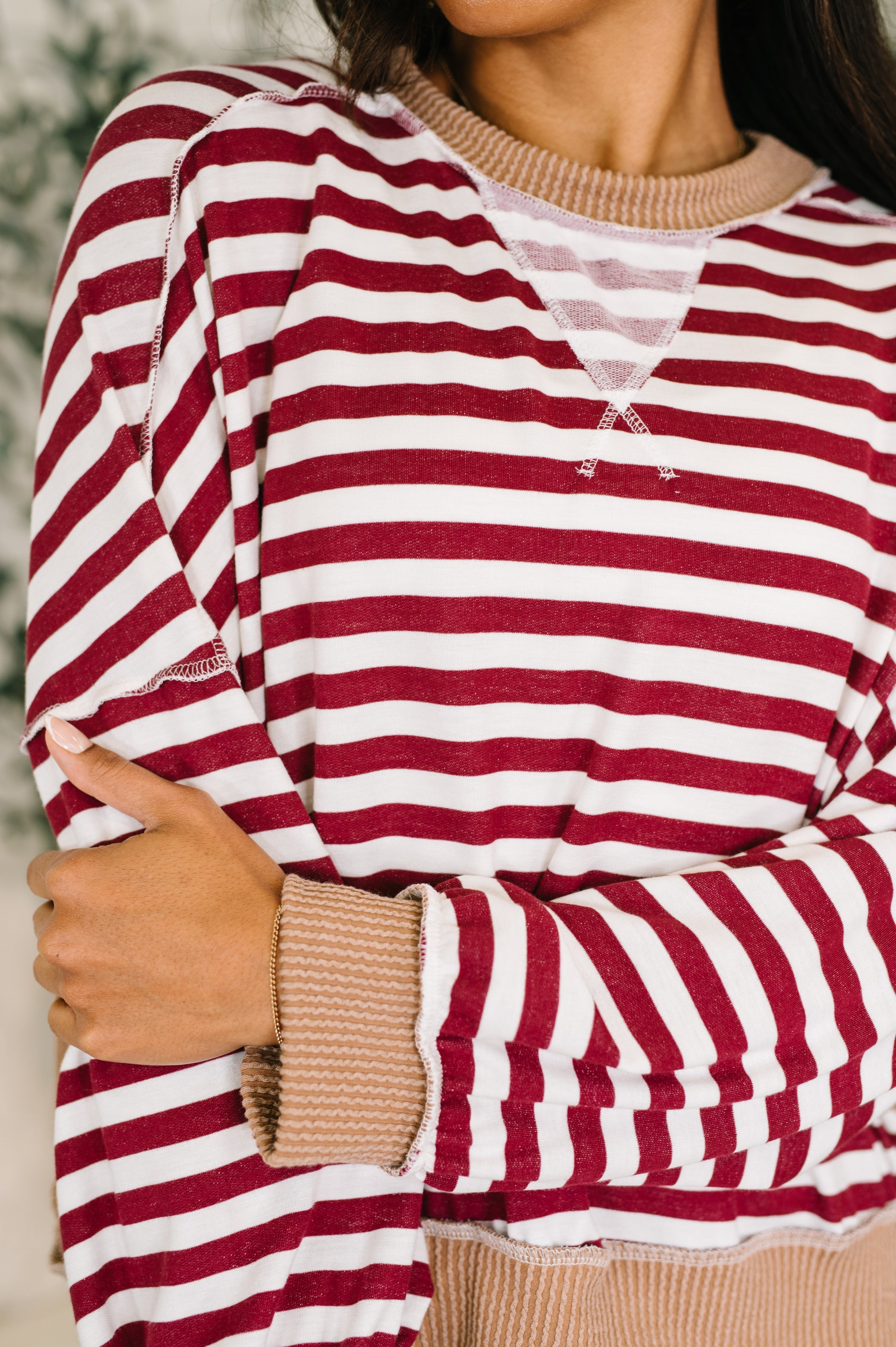 Woman wearing a red and white striped dolman sleeve pullover top with beige trim standing in an indoor setting.