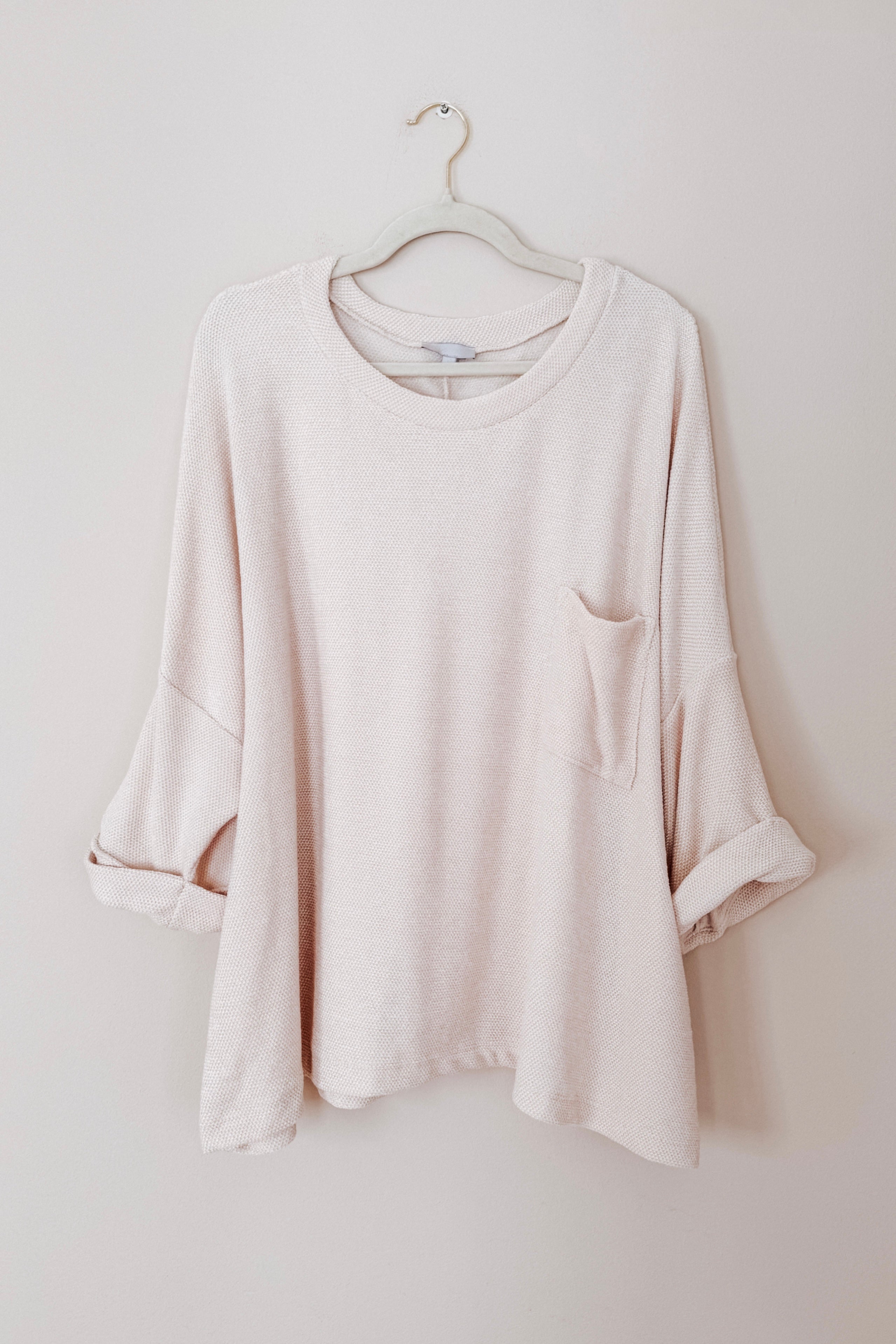 Ivory Thoughts chenille blouse with rolled sleeves and chest pocket hanging on hanger against beige wall