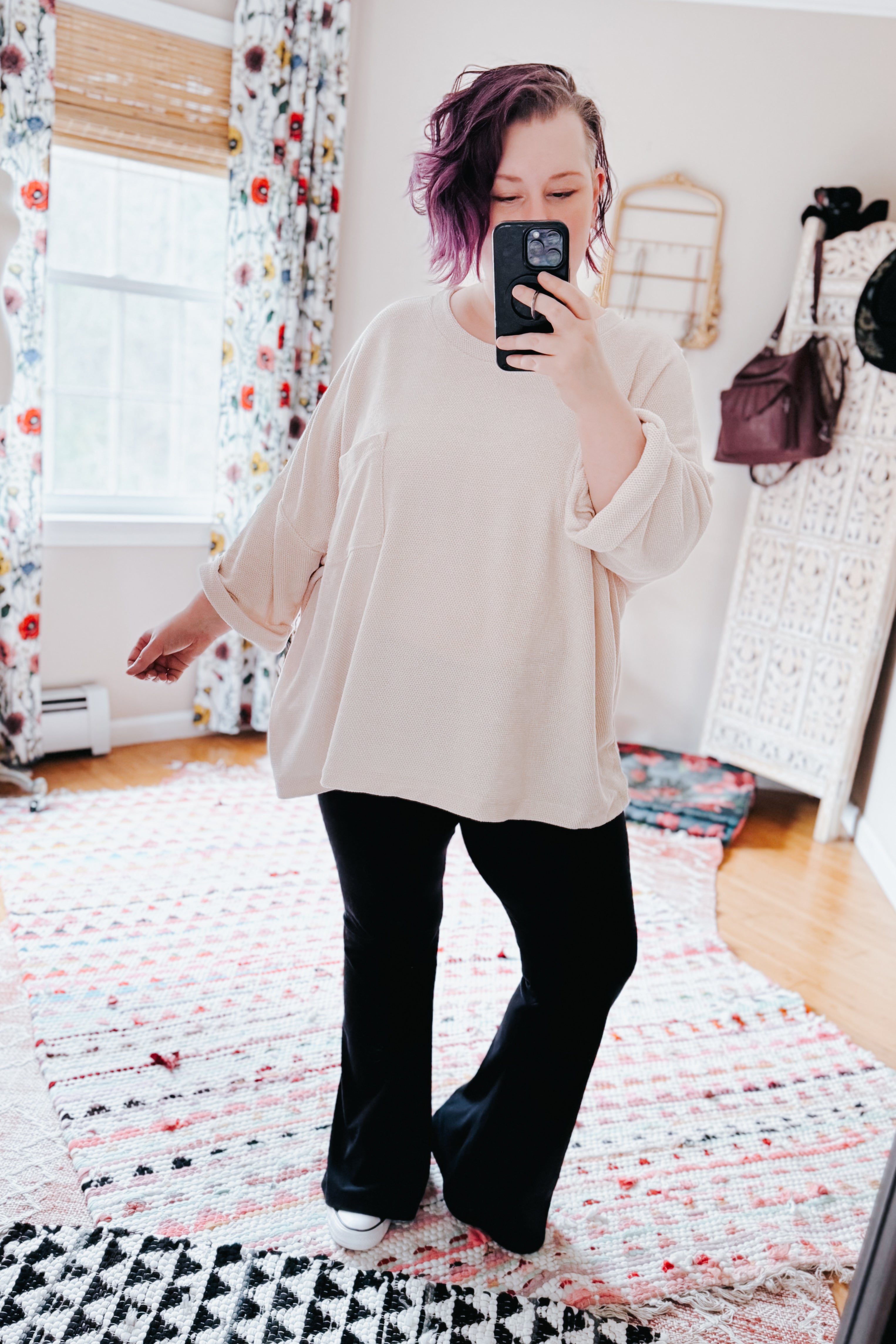 Woman wearing loose ivory Thoughts chenille blouse with rolled sleeves paired with black pants taking mirror selfie indoors