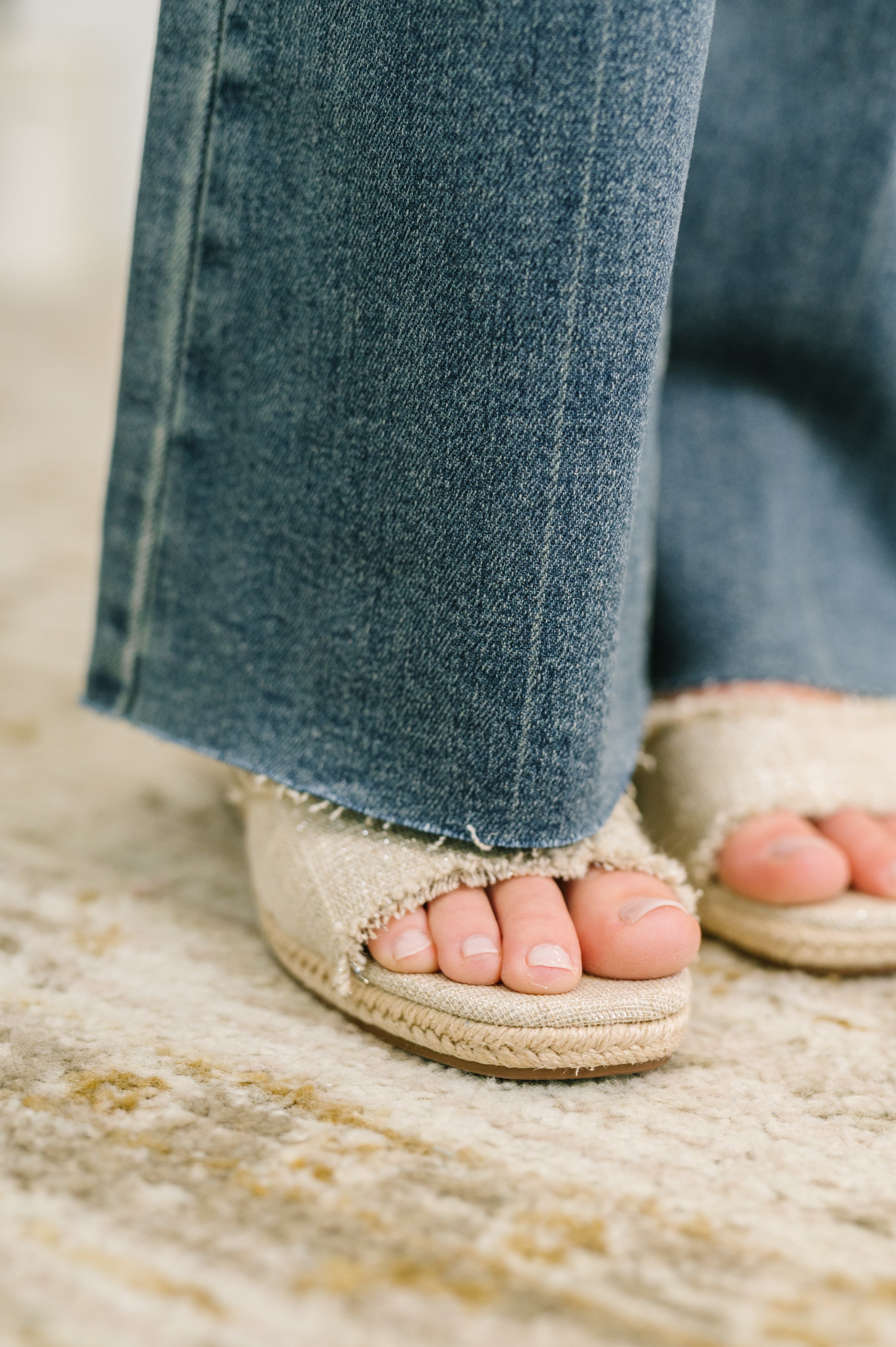 Close-up of blue mid-rise flare jeans hem paired with casual beige open-toe sandals on textured rug surface