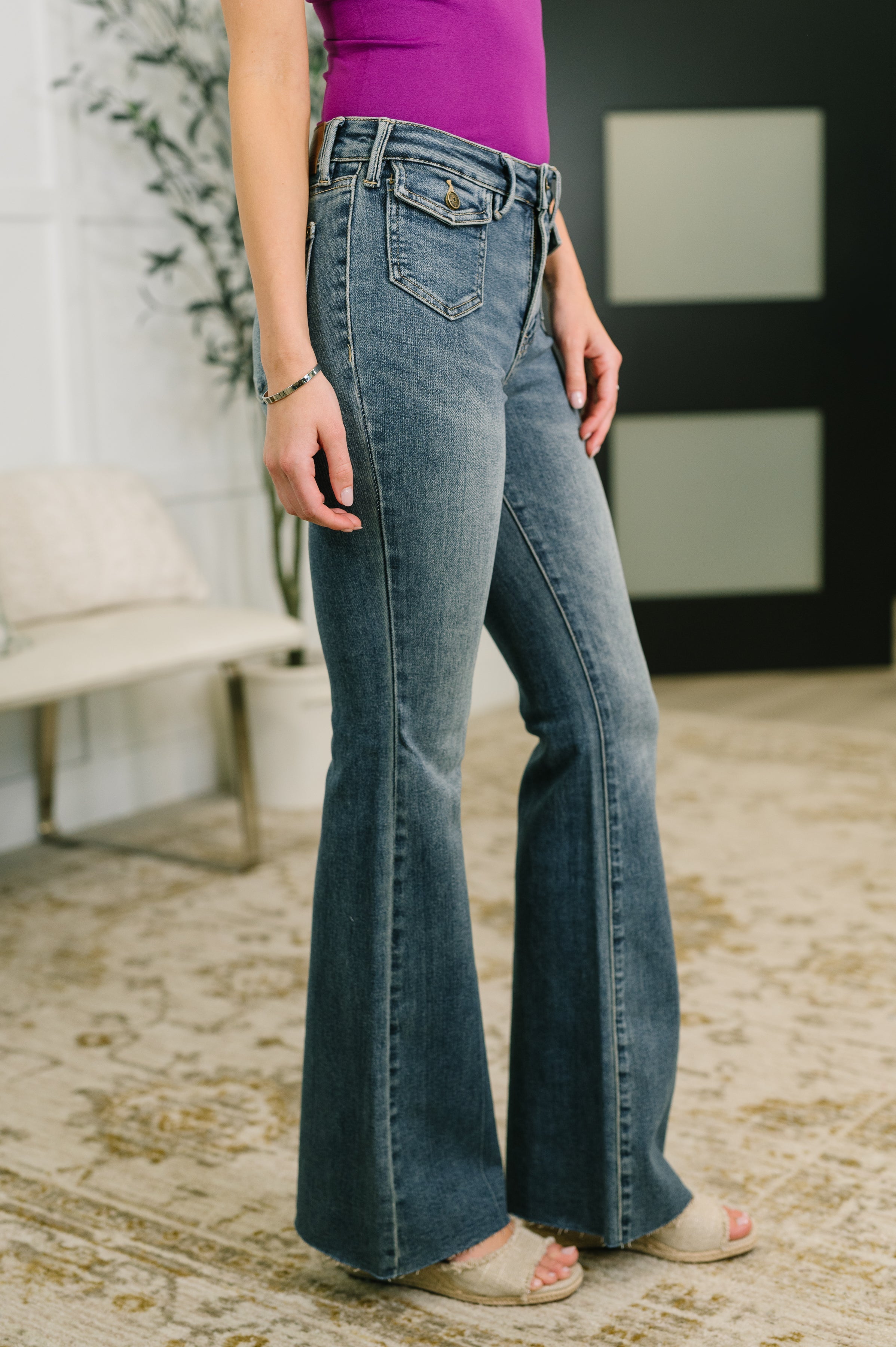 Woman wearing blue flare jeans with front flap pockets paired with mauve top and open-toe sandals indoors