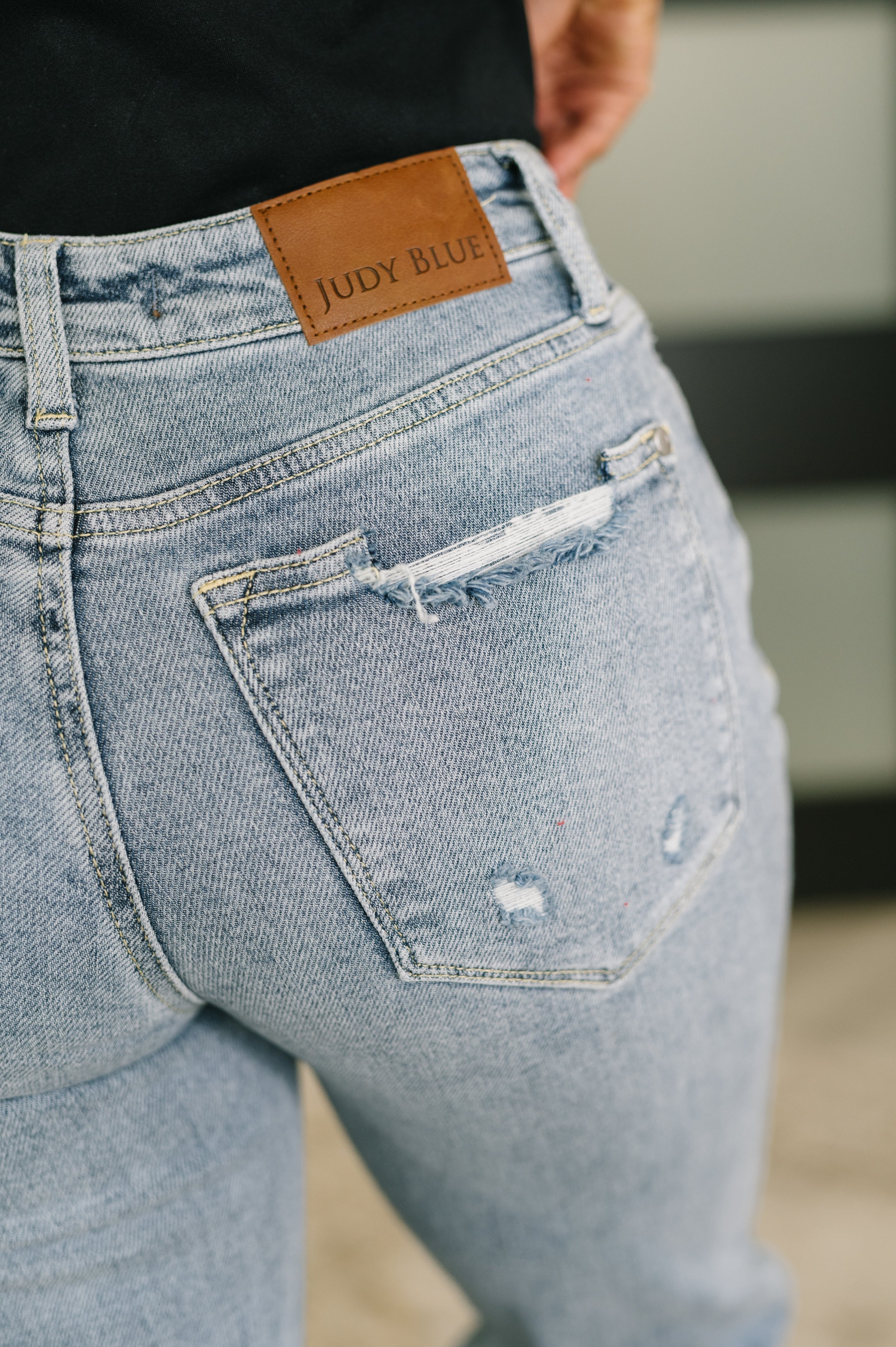 Close-up of distressed back pocket on blue Jade Mid Rise 90's Straight jeans featuring brown Judy Blue label