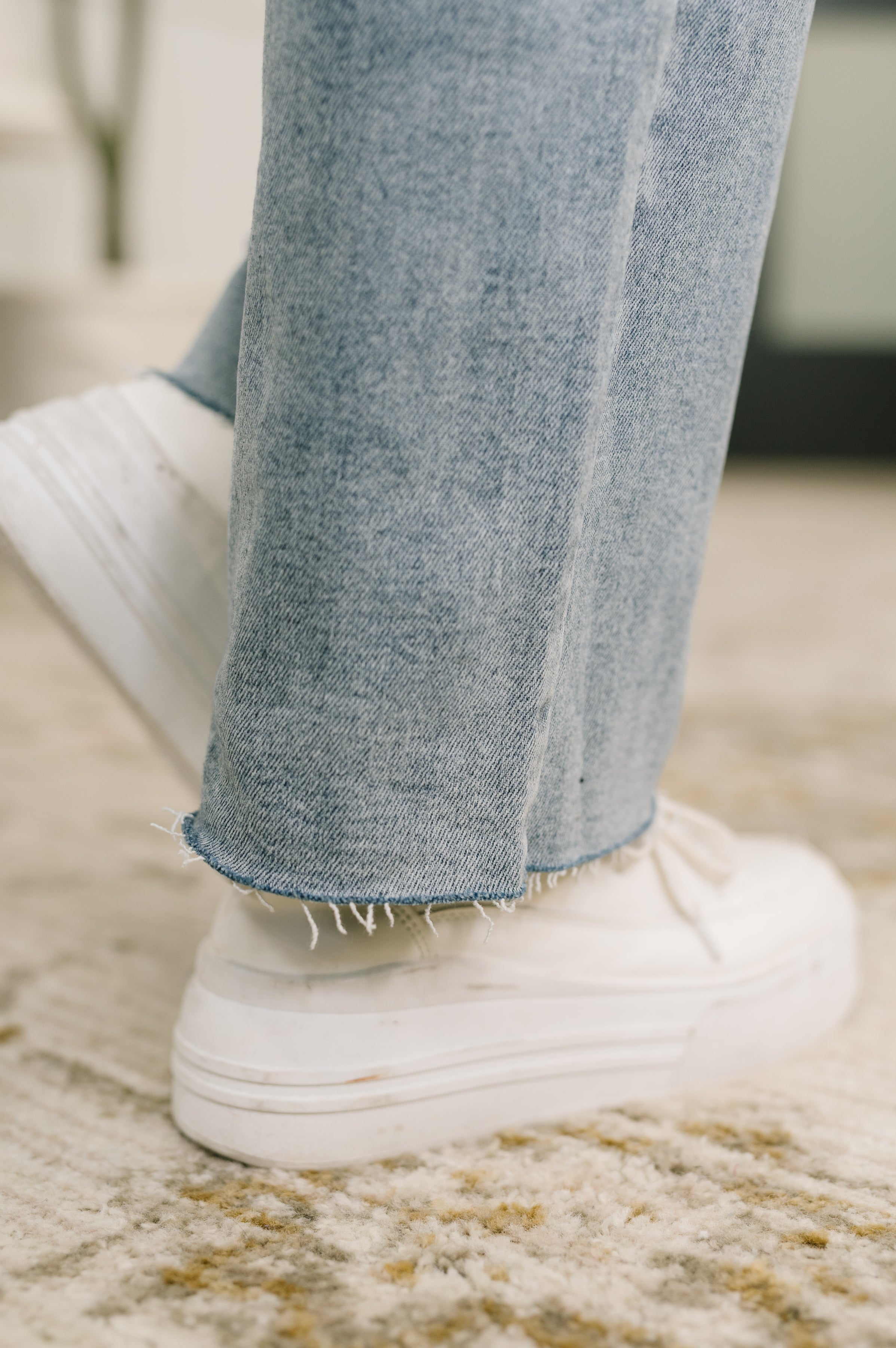 Close-up of hem on blue Jade Mid Rise 90's Straight jeans paired with white platform sneakers indoors