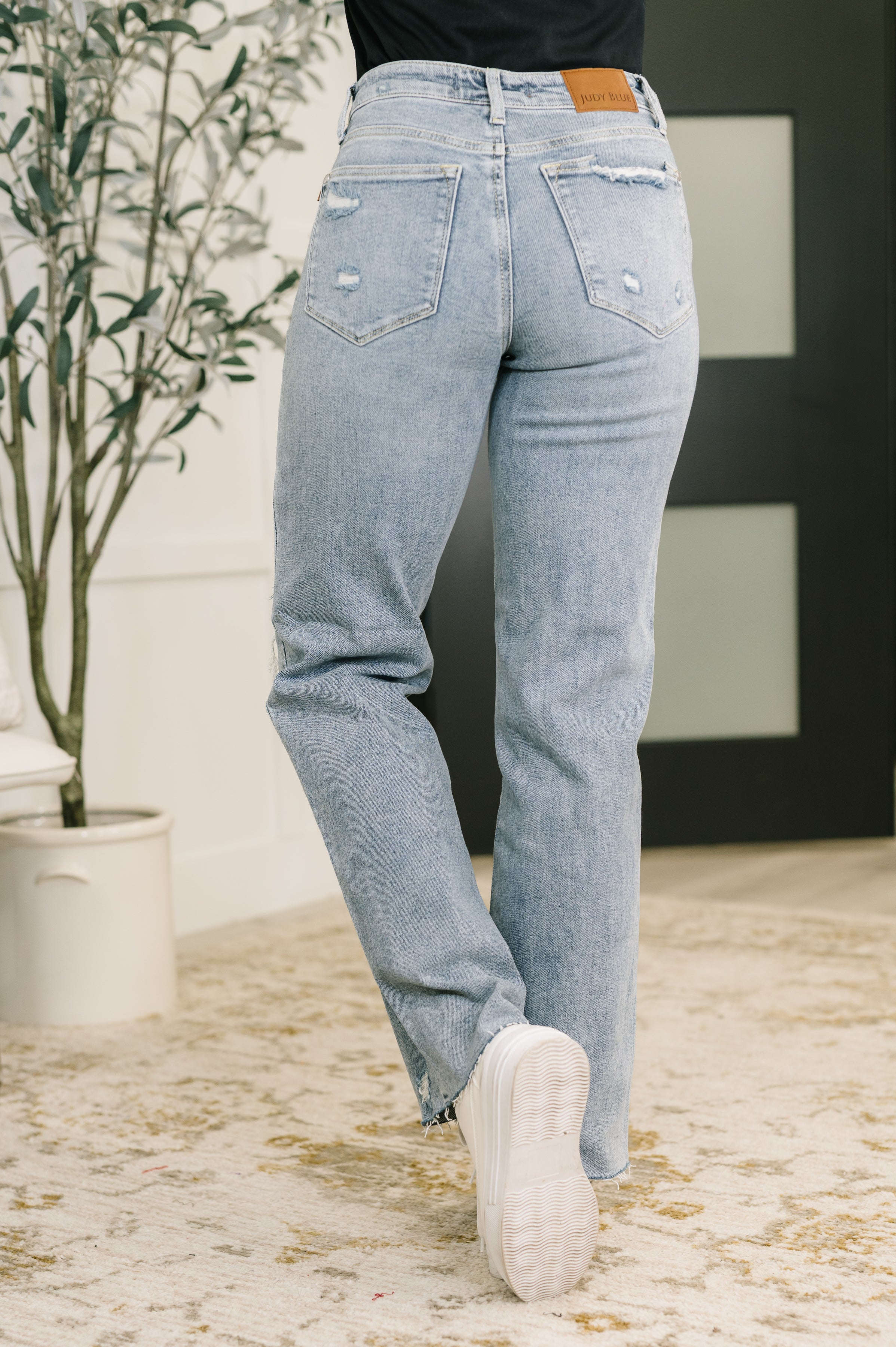 Back view of woman wearing light blue Jade Mid Rise 90's Straight jeans with subtle distressing indoors
