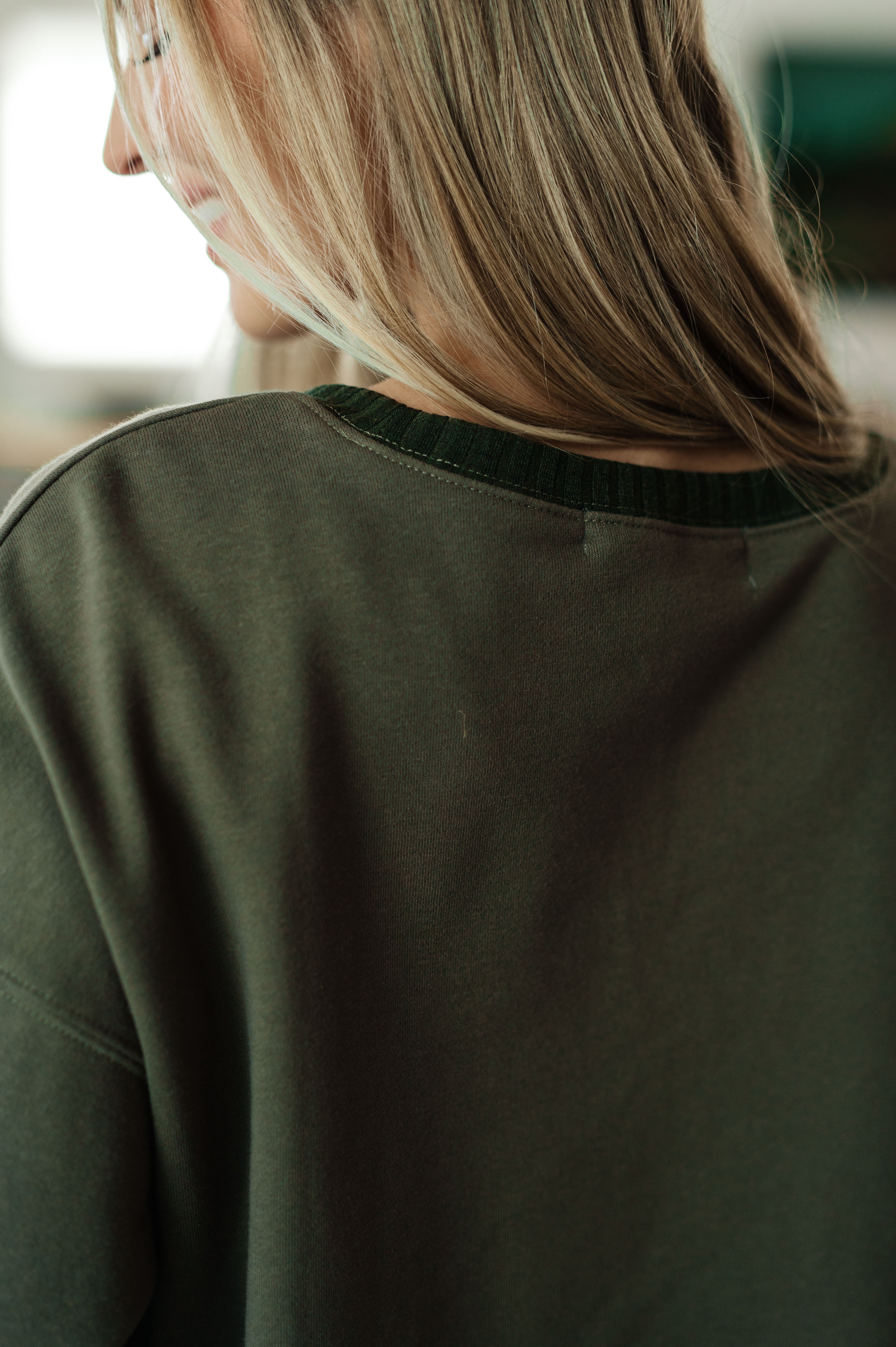 Close-up of back neckline on green Just a Casual Crop Pullover worn by person with long blonde hair indoors
