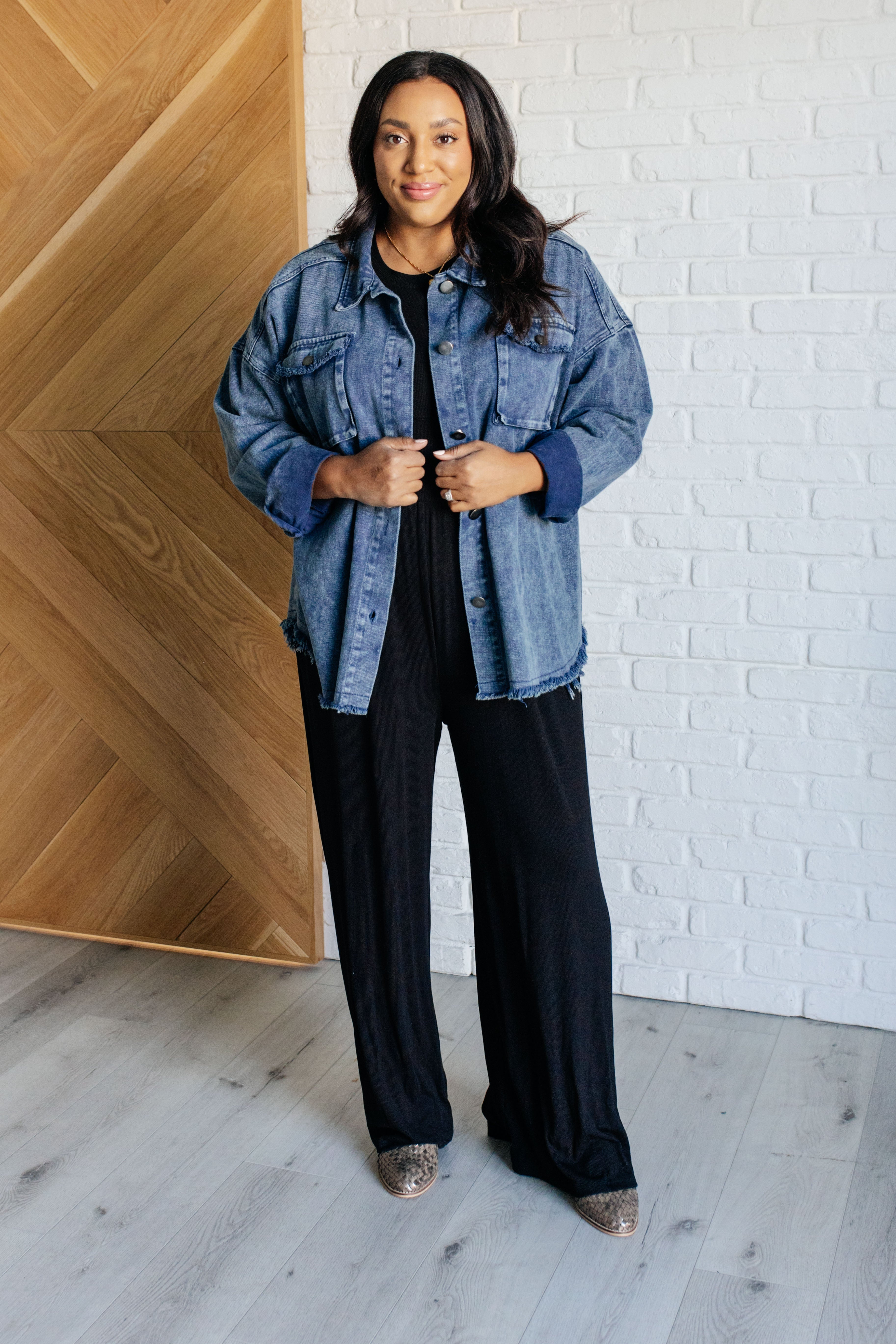 Woman standing indoors wearing blue Just In Case Mineral Wash Shacket with button front and frayed hem over black outfit