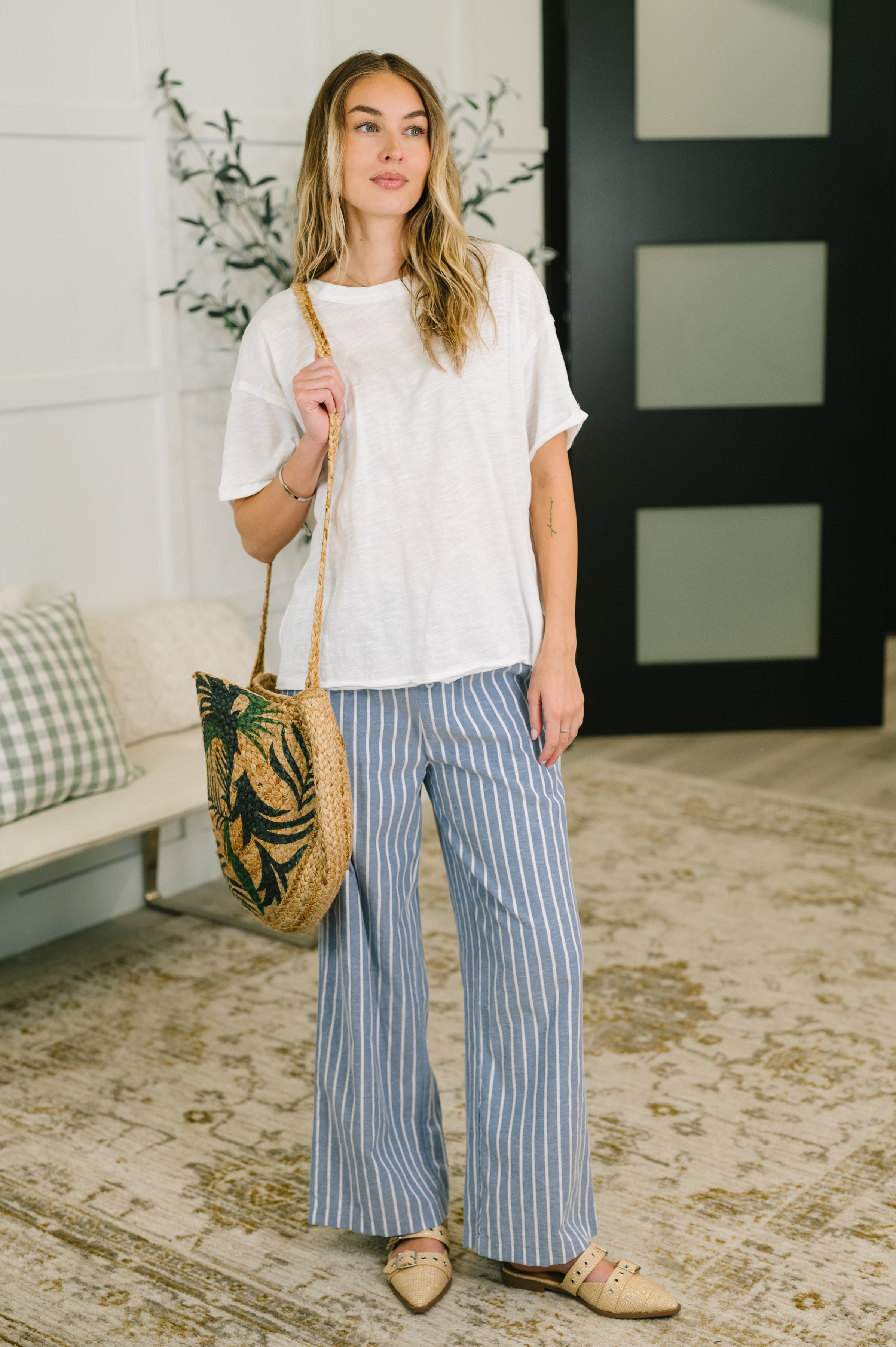 Woman wearing relaxed ivory tee with striped wide-leg pants and carrying woven tote bag indoors