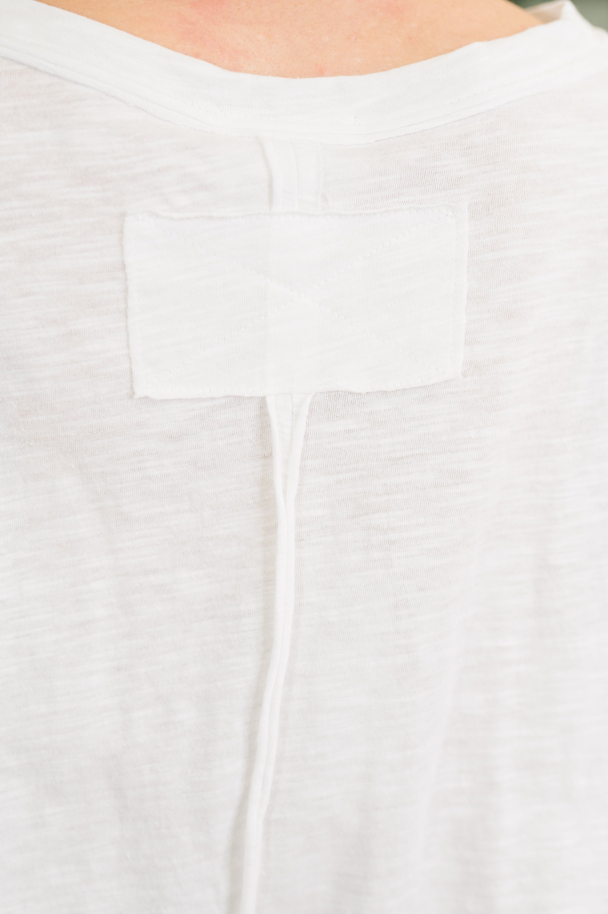 Close-up of ivory heather fabric with vertical seam and rectangular stitched patch detail on soft cotton tee