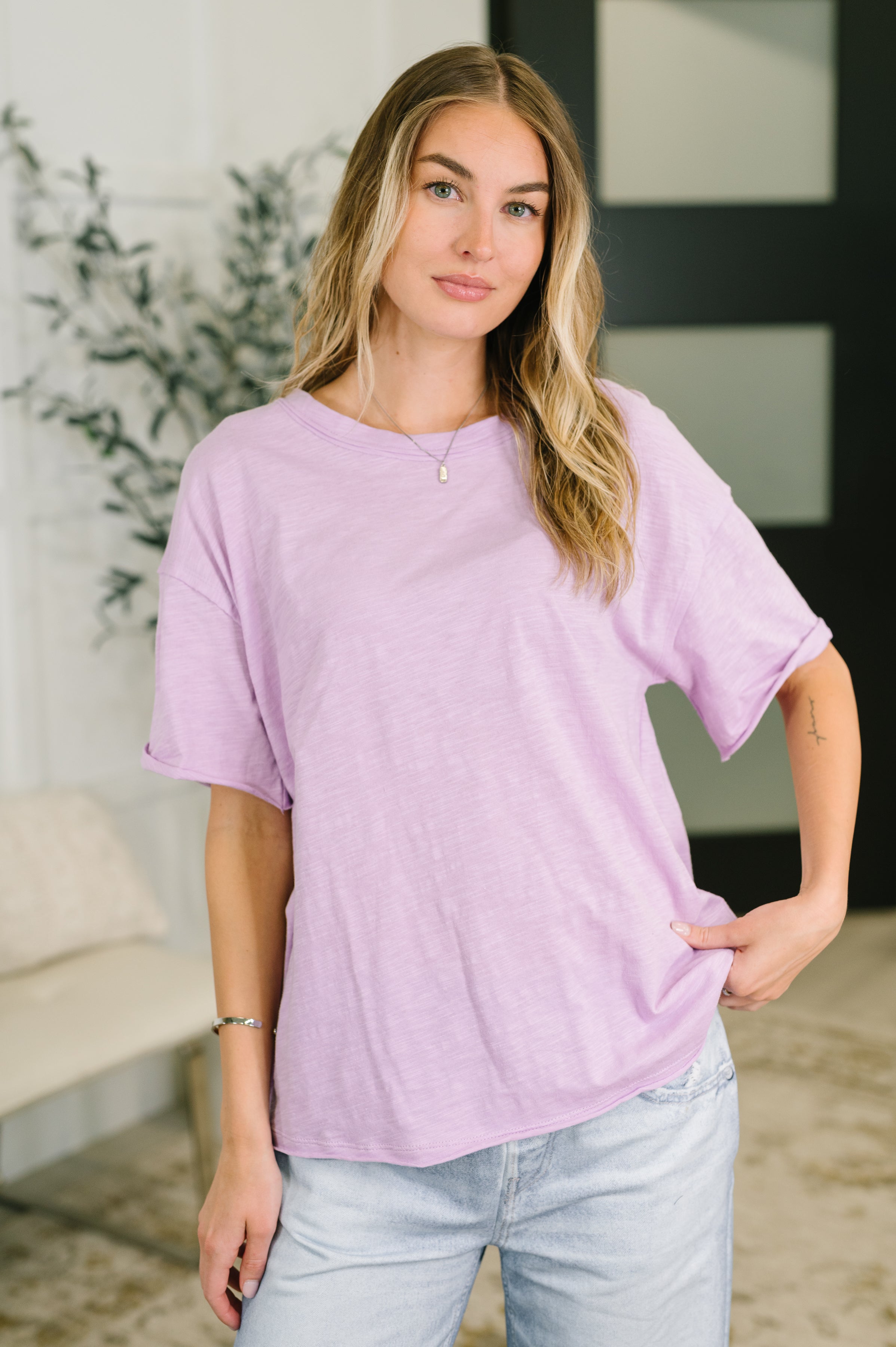 Woman wearing a lilac relaxed-fit tee with rolled sleeves paired with light washed jeans in casual indoor setting