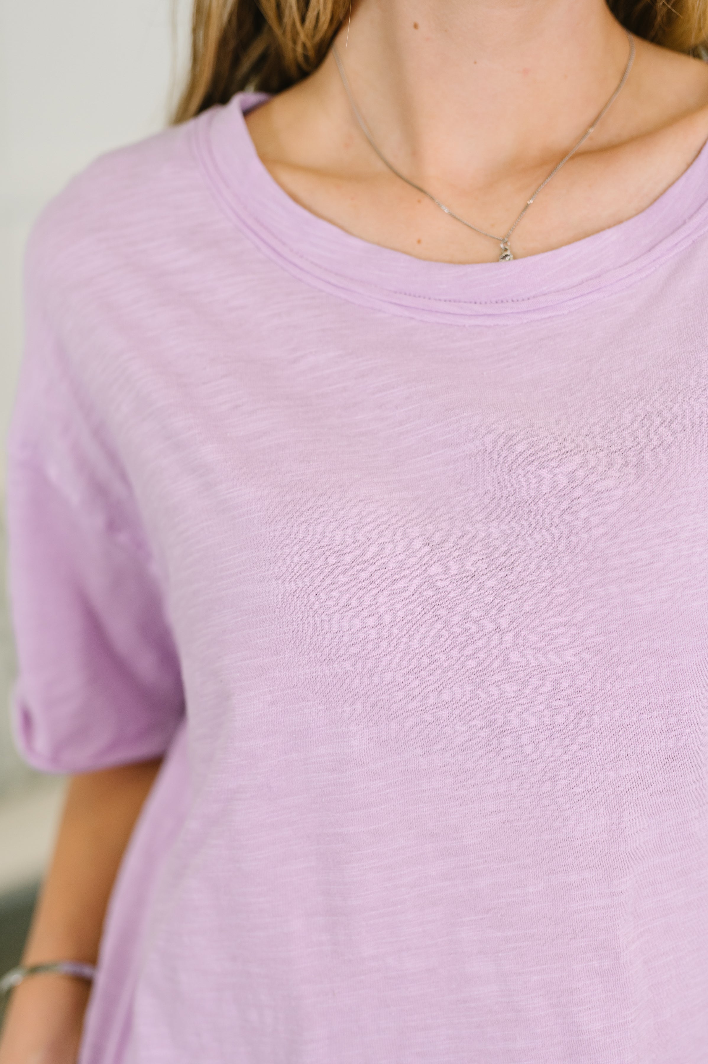 Close-up of a relaxed lilac heather tee worn with a delicate necklace and silver bracelet, showcasing soft fabric texture
