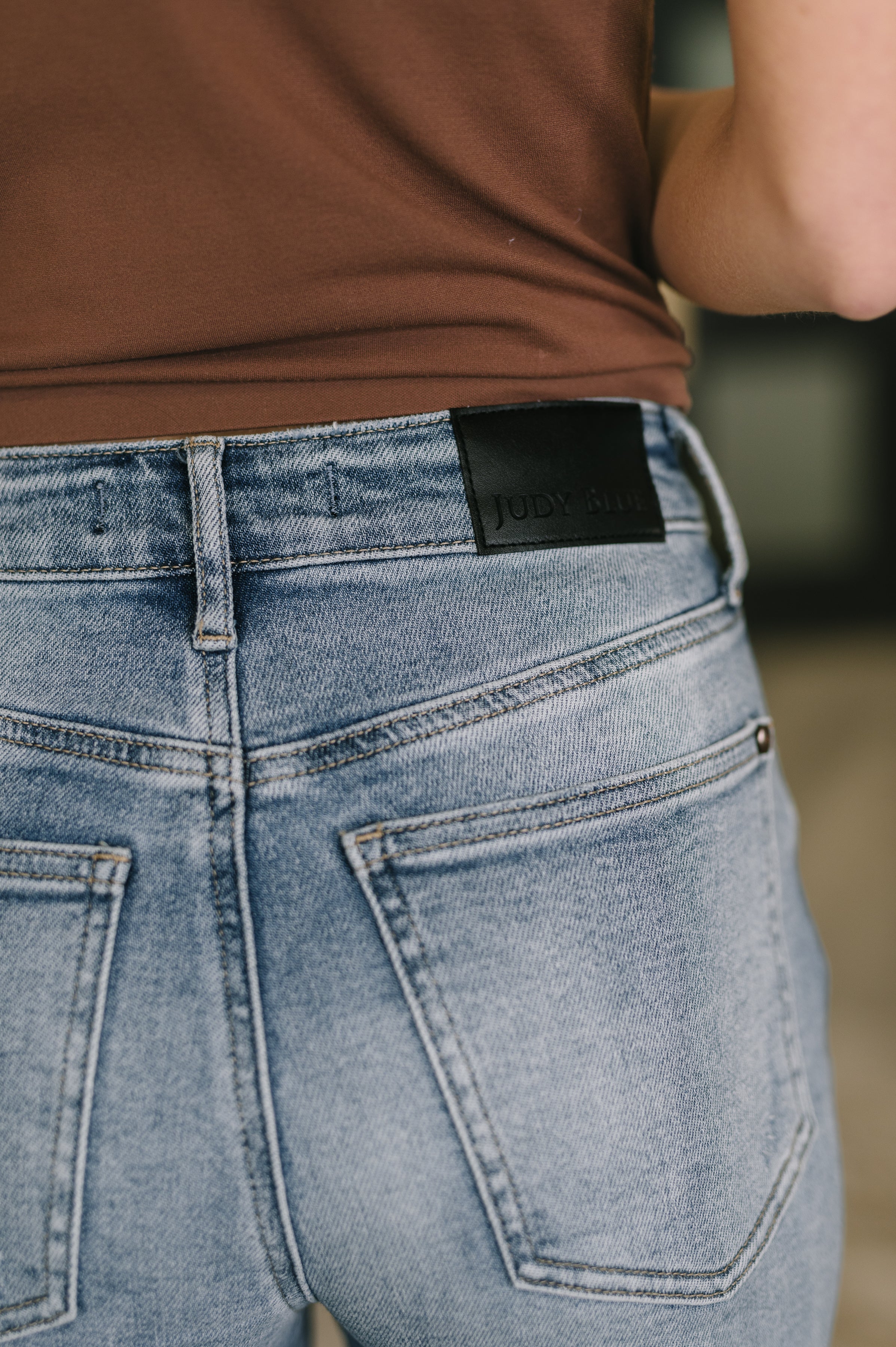 Close-up of light wash high-rise rigid jeans with back pockets and black leather brand patch worn indoors