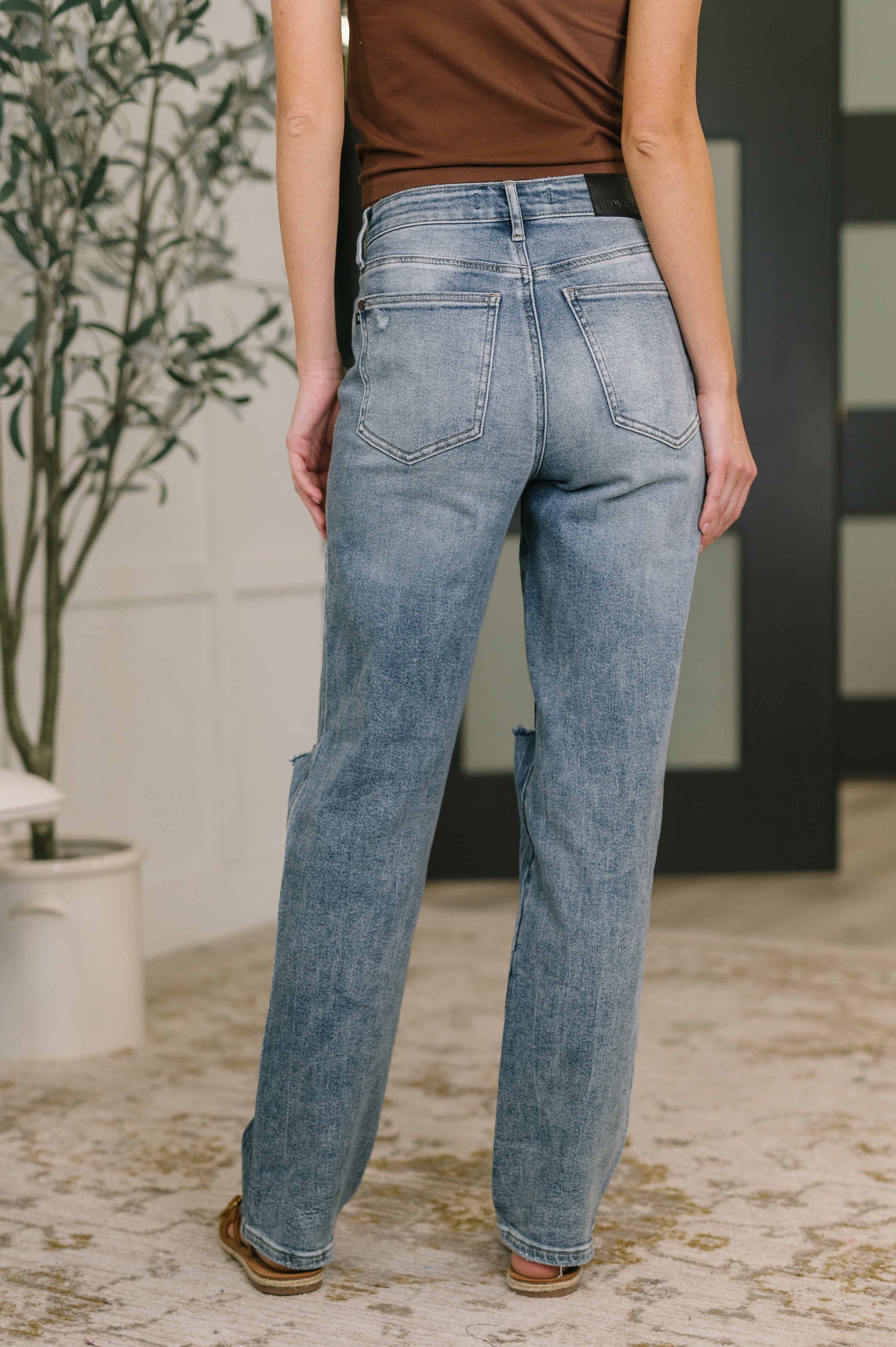 Back view of woman wearing light wash high-rise rigid straight jeans with slight distressing indoors