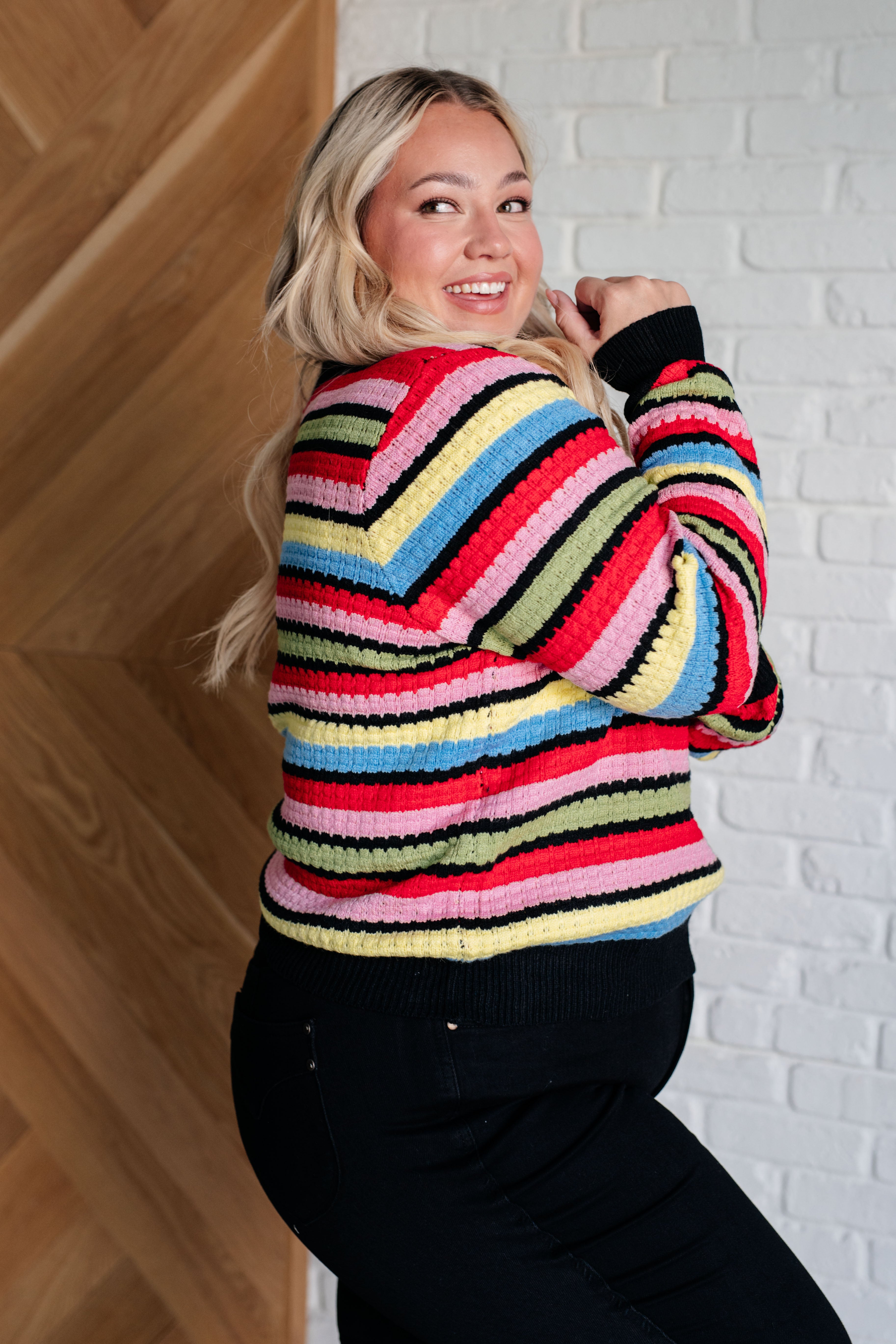 Smiling woman indoors wearing multicolor Keep Dreaming Striped Sweater with ribbed knit and black cuffs and hem